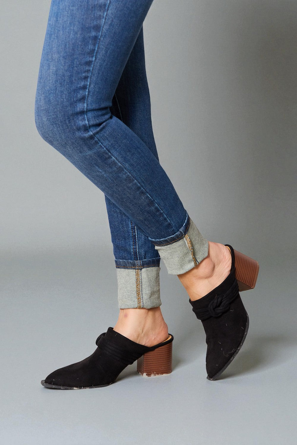 Person wearing blue jeans and black open-toe shoes on a gray background