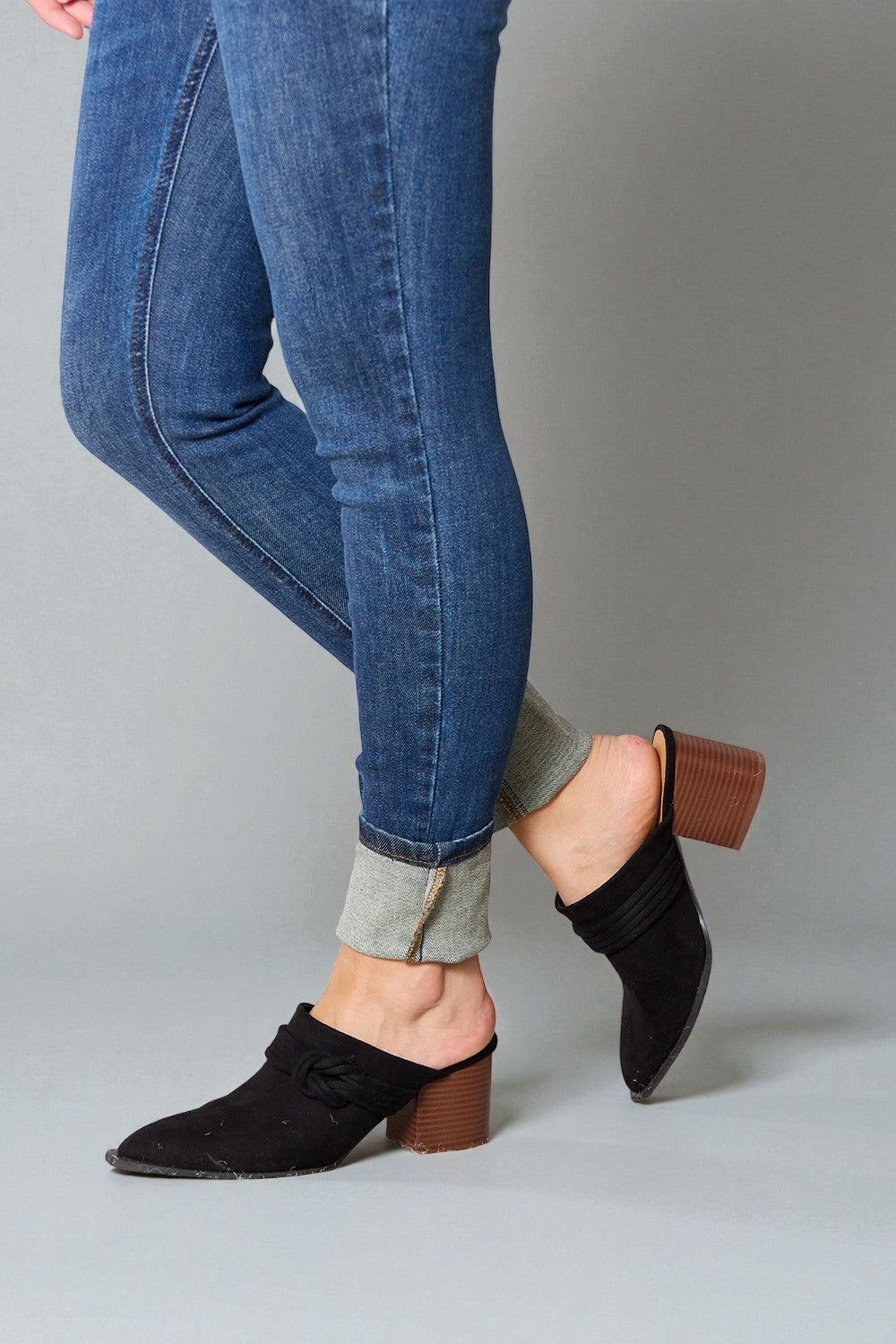 Person wearing blue jeans with rolled-up cuffs and black block-heel shoes on a gray background