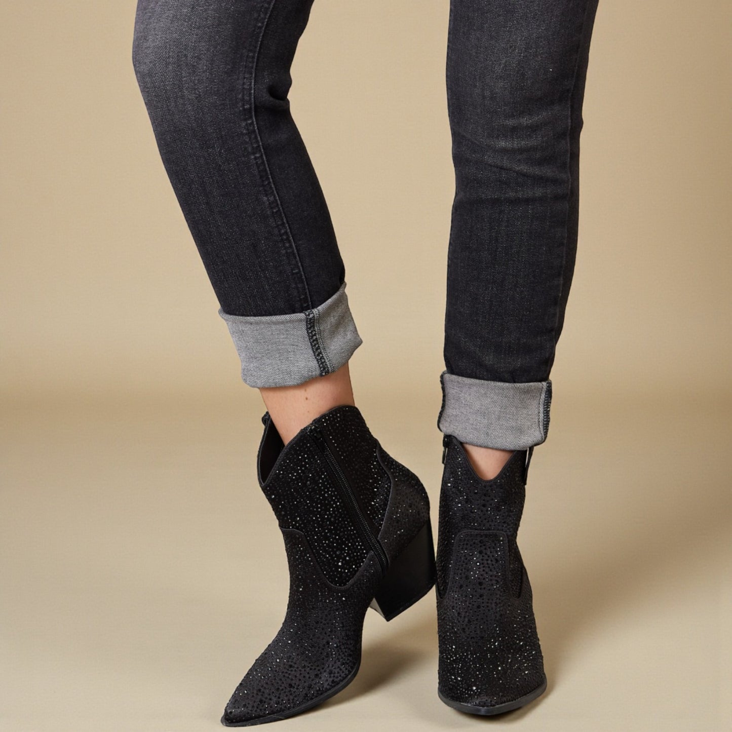 Black glittery ankle boots worn with black jeans on a beige background
