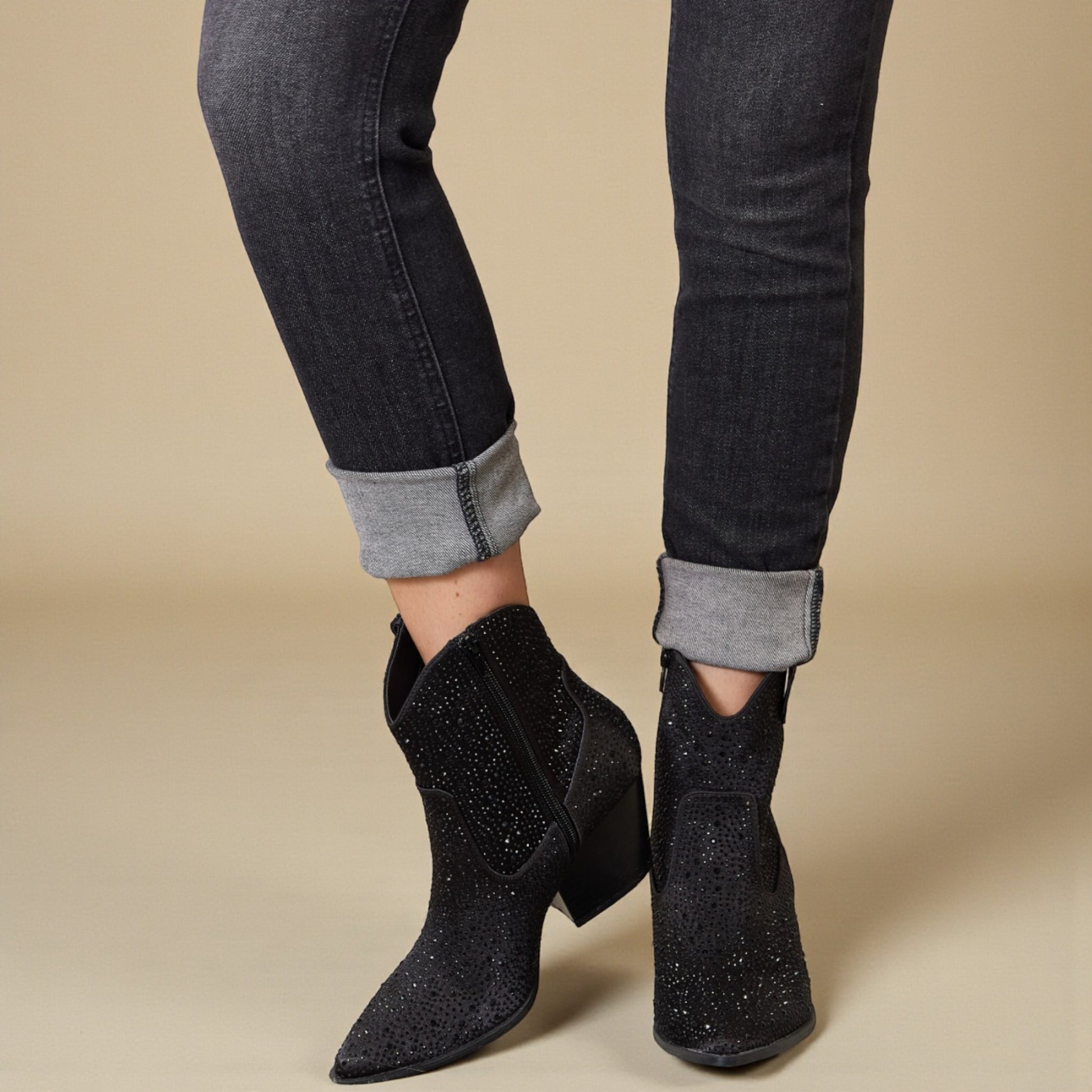 Black glittery ankle boots worn with black jeans on a beige background