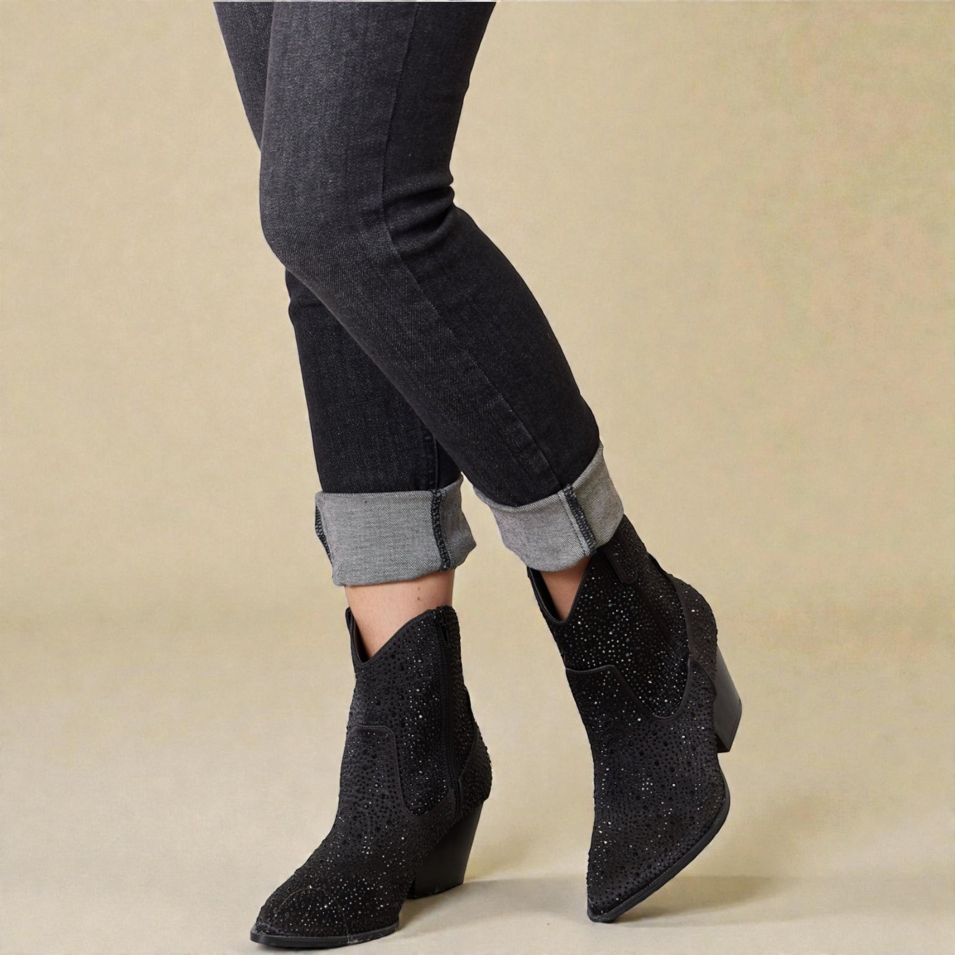 Black ankle boots worn with rolled-up jeans on a beige background