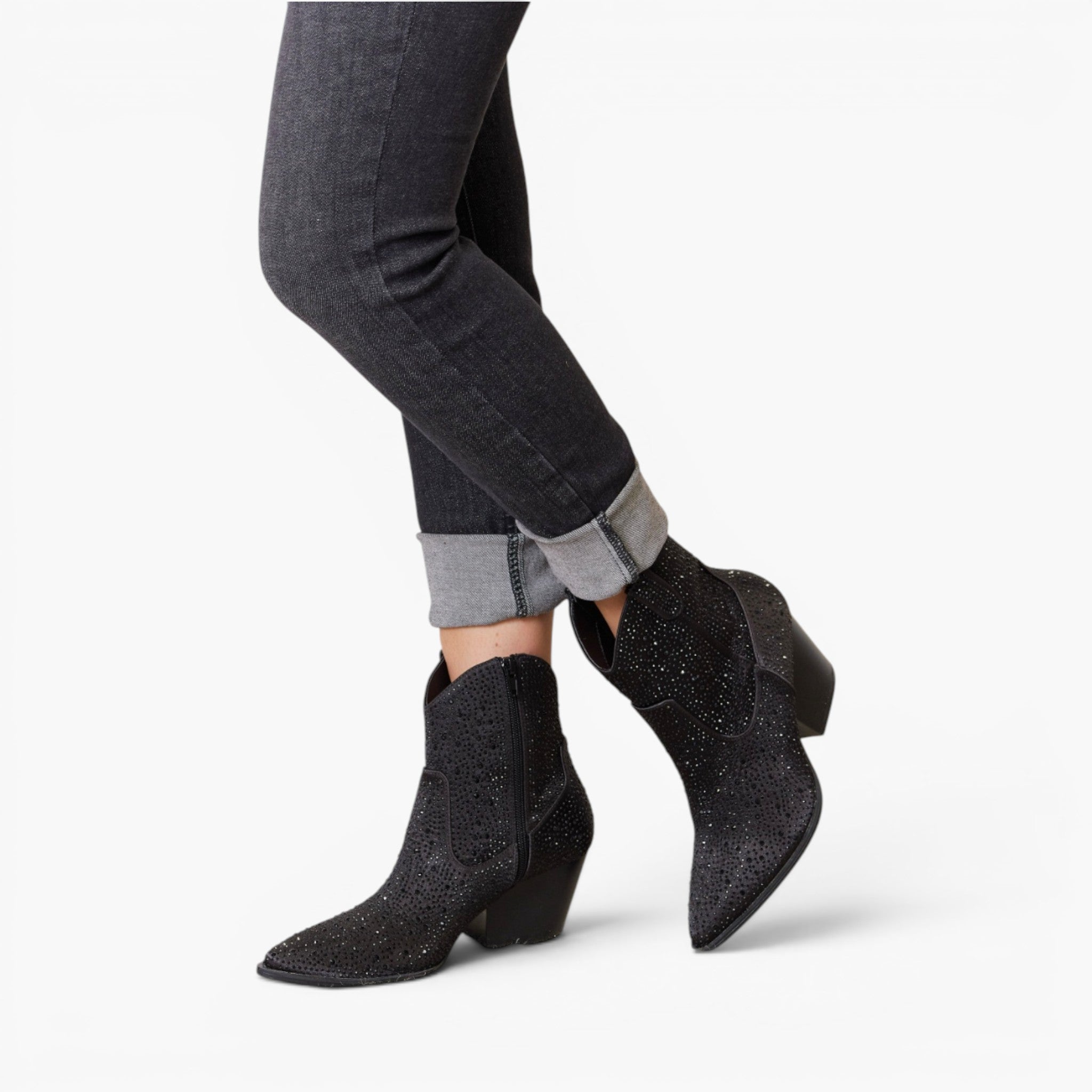 Black glitter ankle boots with pointed toes and low block heels, shown on a model wearing dark gray cuffed jeans against a white studio background.