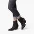 Black glitter ankle boots with pointed toes and low block heels, shown on a model wearing dark gray cuffed jeans against a white studio background.