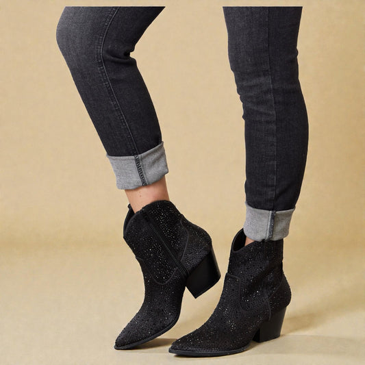 Black glittery ankle boots worn with black jeans on a beige background