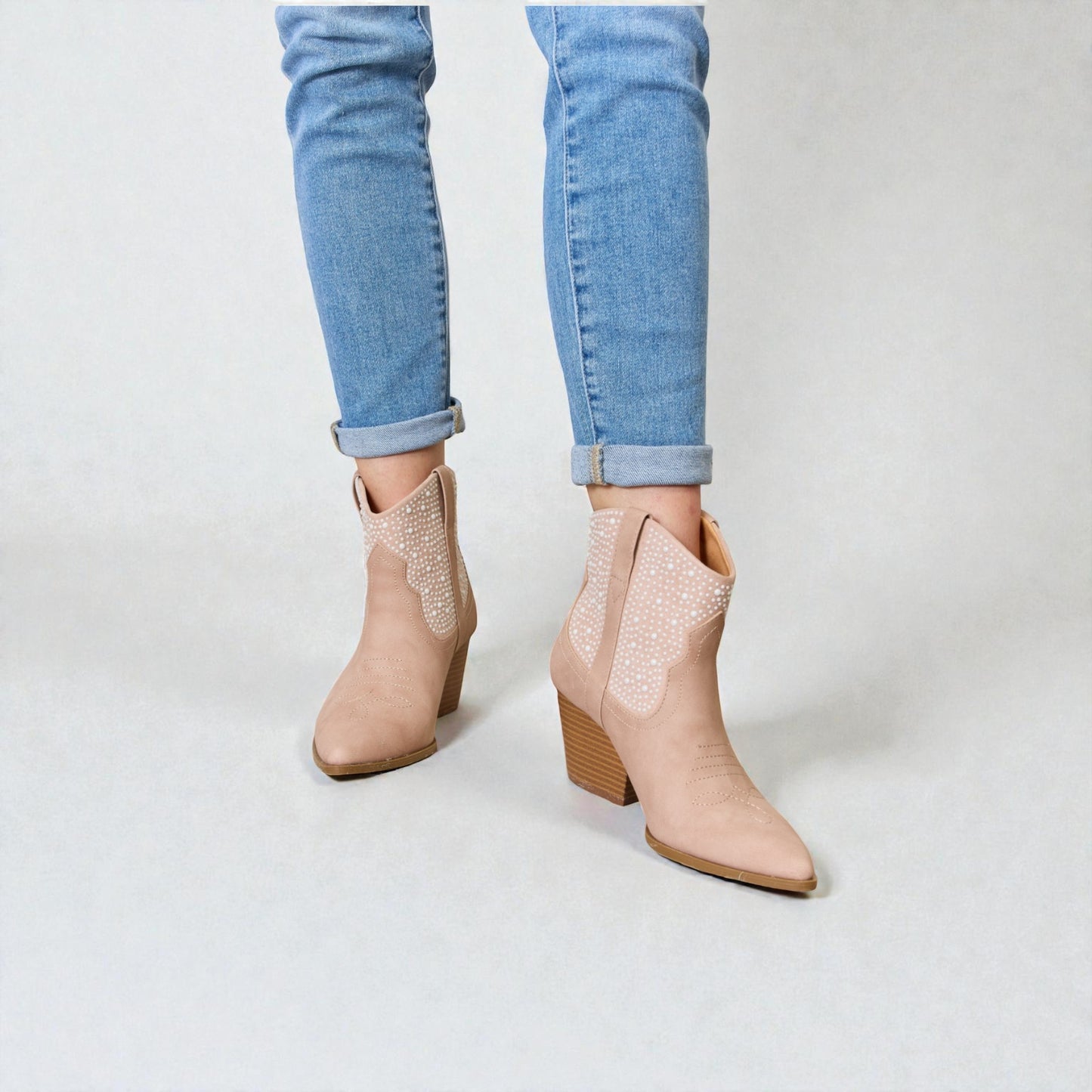 Beige ankle boots worn with light blue jeans on a white background