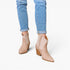 A person wearing light blue cuffed jeans and beige pointed-toe ankle boots with textured side panels, shown against a plain light gray studio background.