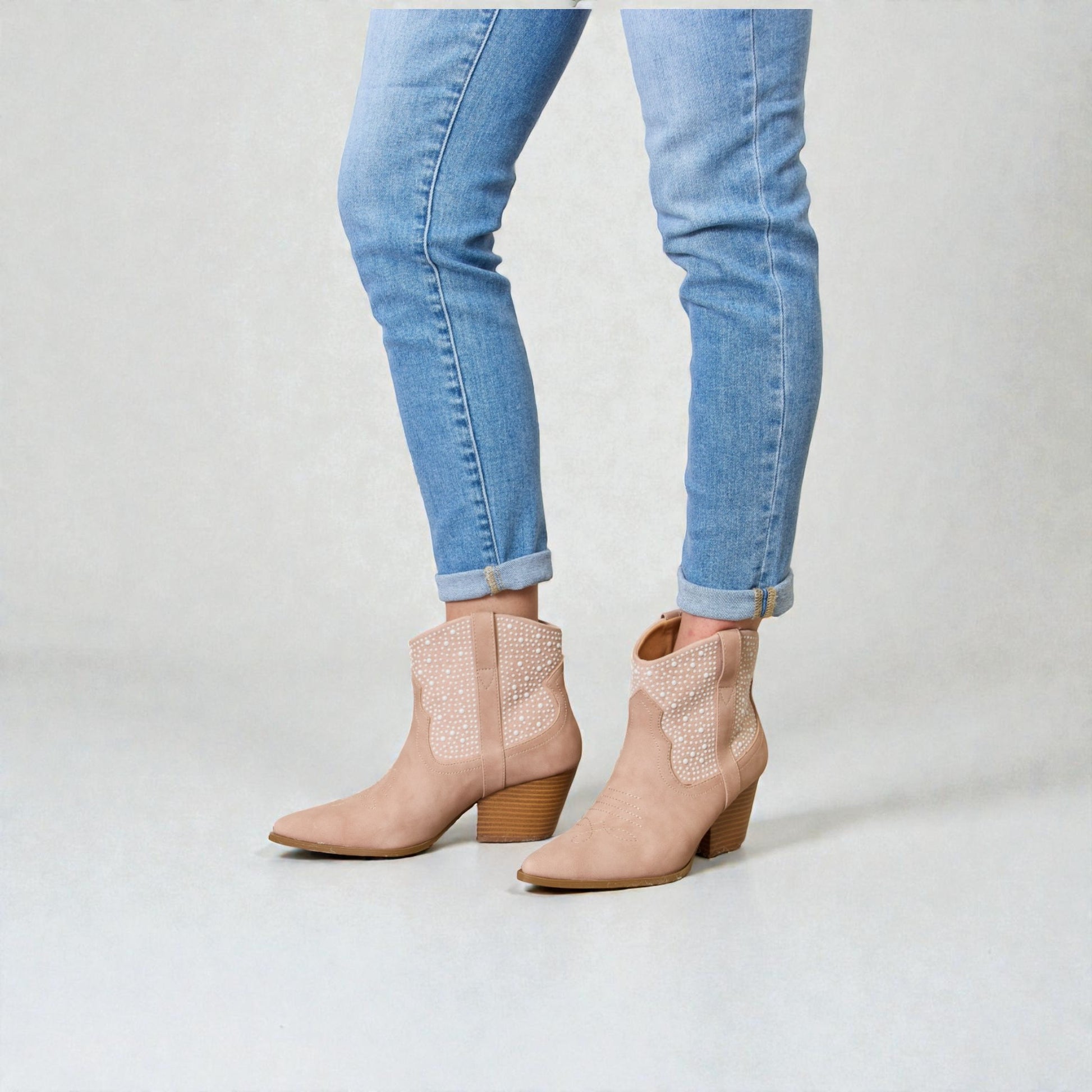 Beige ankle boots worn with light blue jeans on a plain background