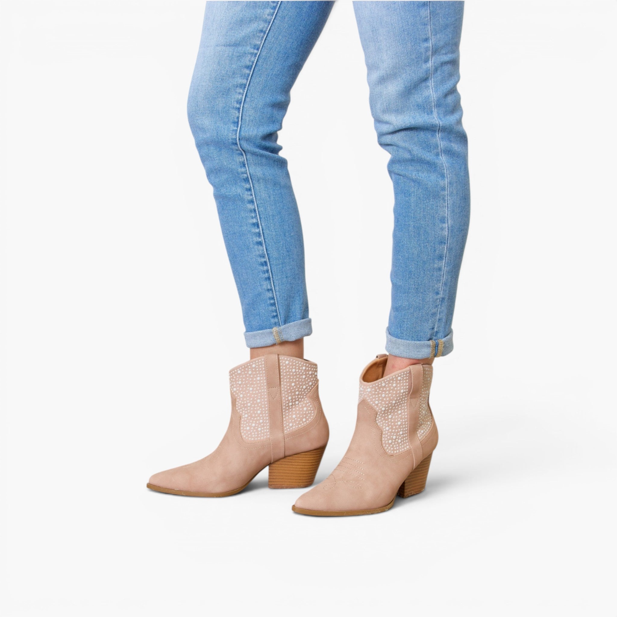 A person wearing light blue skinny jeans and beige western-style ankle boots with rhinestone embellishments on the shafts, shown against a plain white studio background.