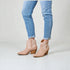 Beige ankle boots worn with light blue jeans on a plain background