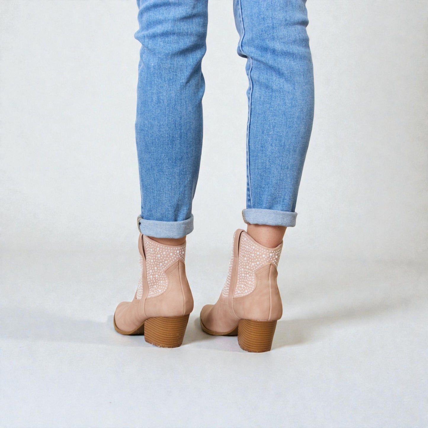 Beige ankle boots with brown soles worn with light blue jeans on a white background