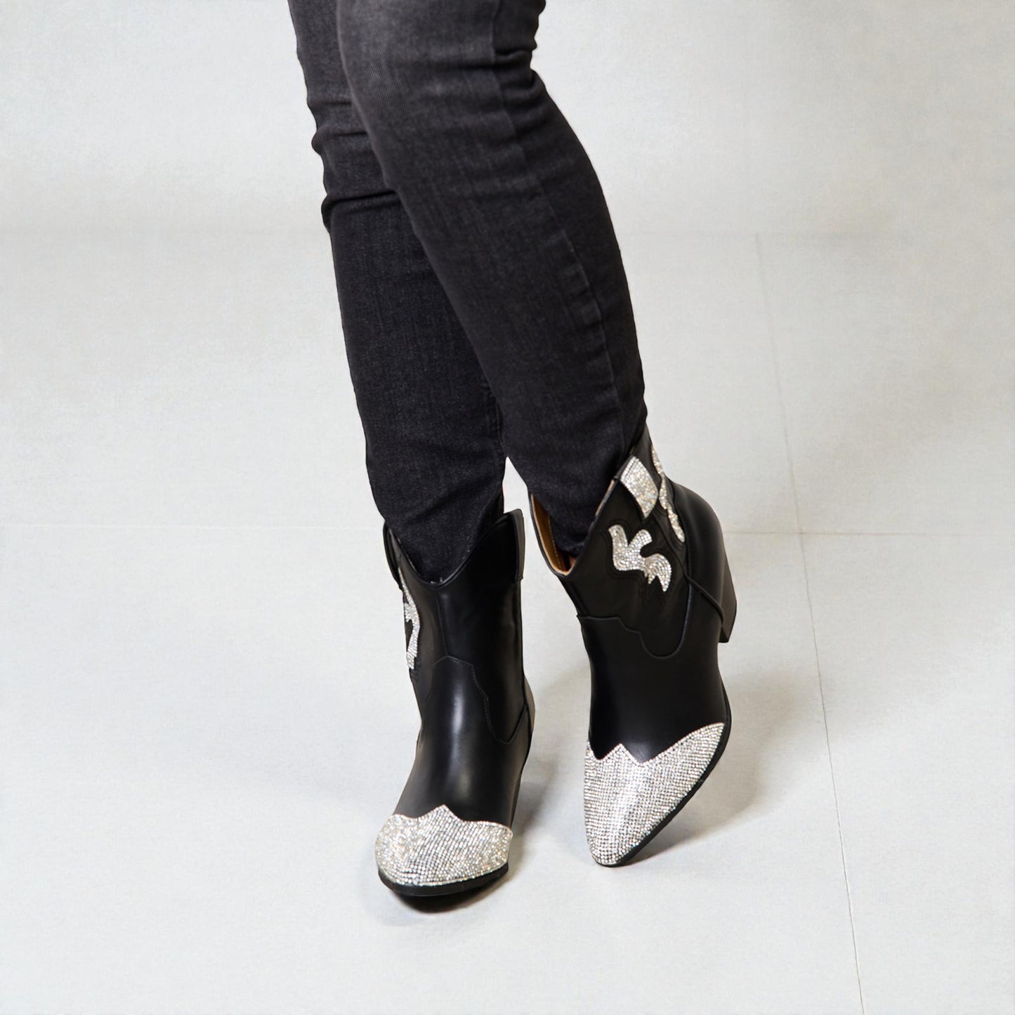 Black ankle boots with silver glittery toes worn with black pants on a white background