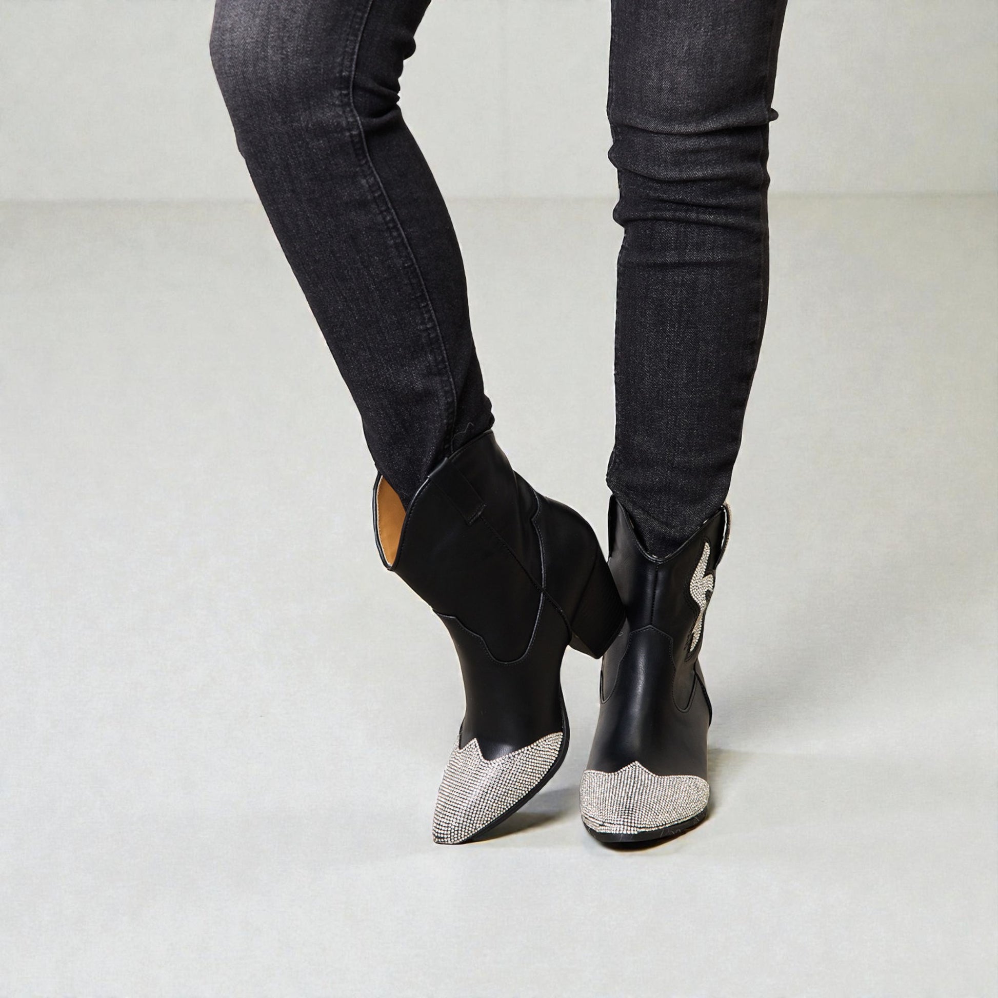 Black pointed-toe boots with patterned soles worn with black jeans on a light gray background