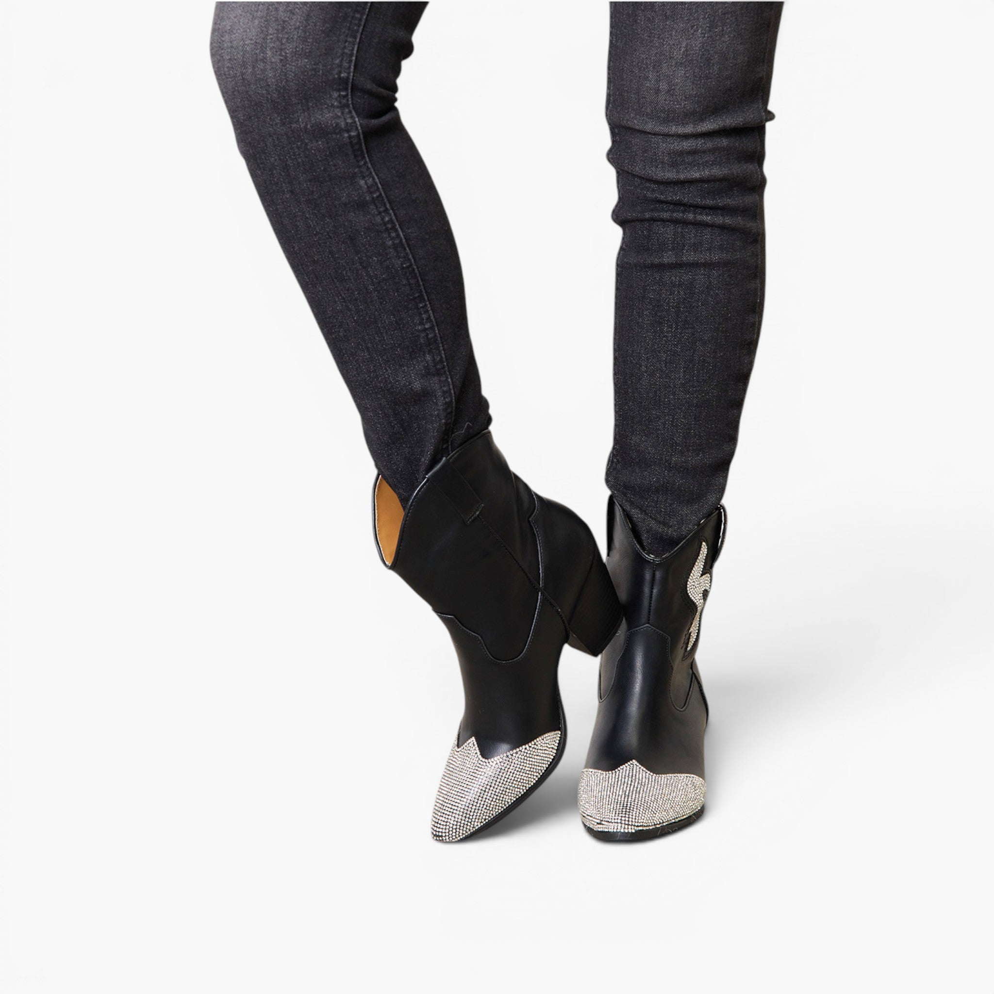 Black ankle boots with silver glitter pointed toes, shown on a model wearing dark gray skinny jeans against a light gray background.