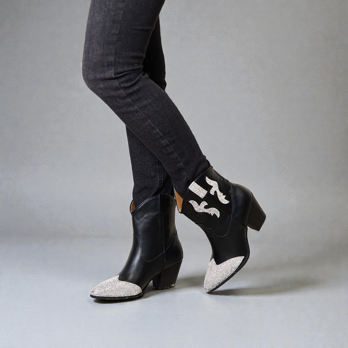 Black ankle boots with decorative white patterns worn with gray jeans on a neutral background