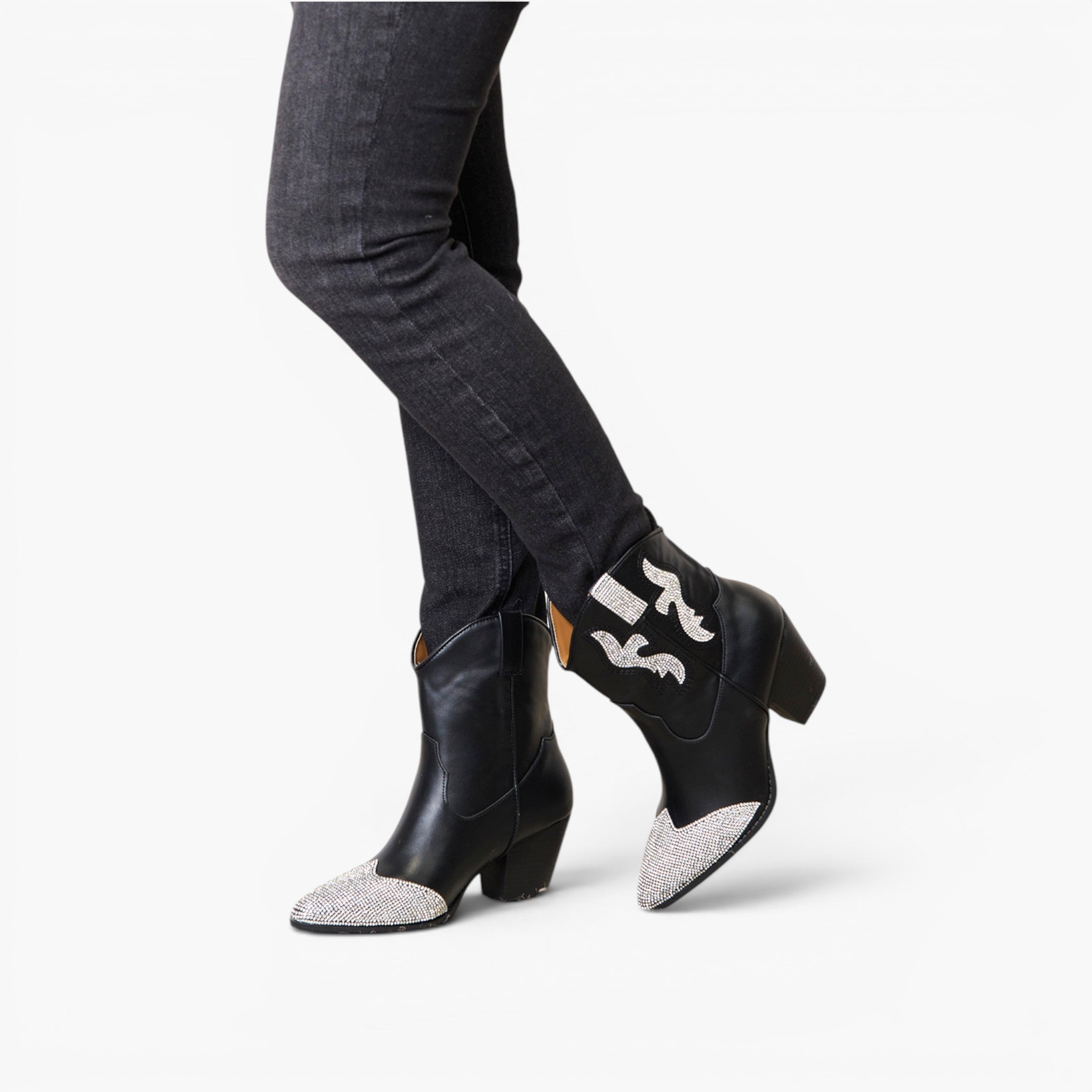 Black leather ankle boots with silver glitter pointed toes and white embroidered bat details, shown on a model wearing dark gray skinny jeans against a white studio background.