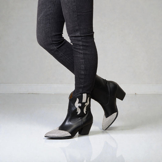 Black ankle boots with silver embellishments worn with black jeans on a light gray background