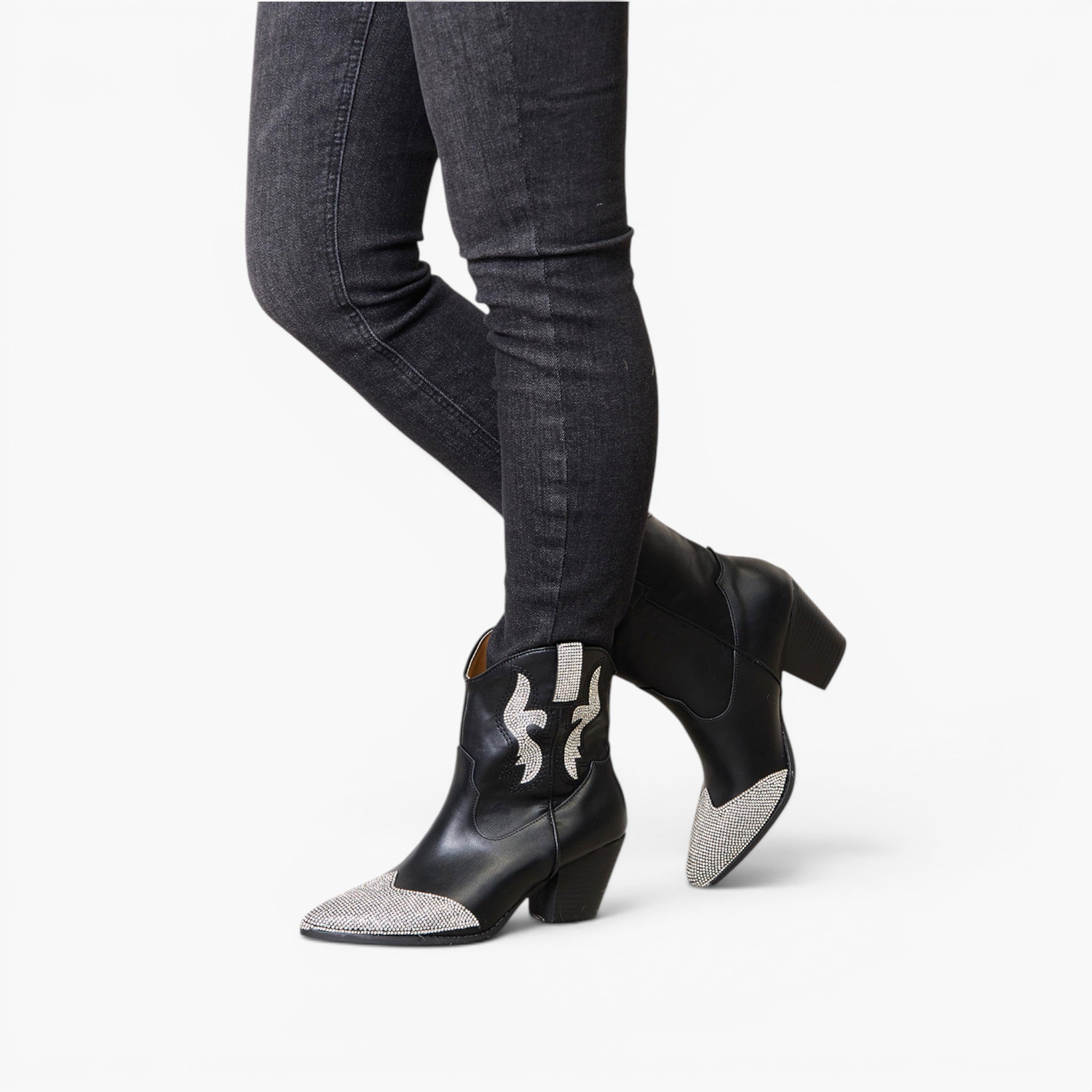 Black leather cowboy boots with silver glitter toe caps and western-style stitching, shown on a model wearing dark gray skinny jeans against a white studio background.