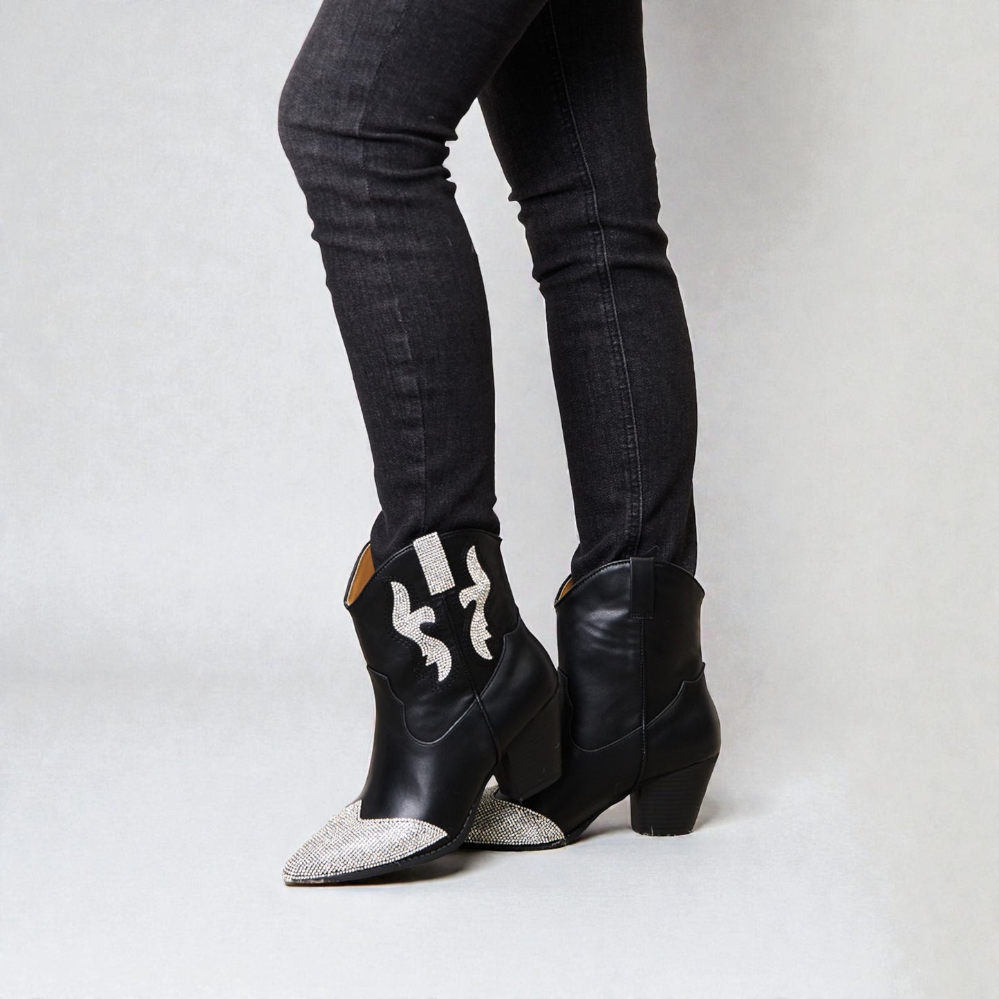 Black cowboy boots with silver embellishments worn with black jeans on a white background