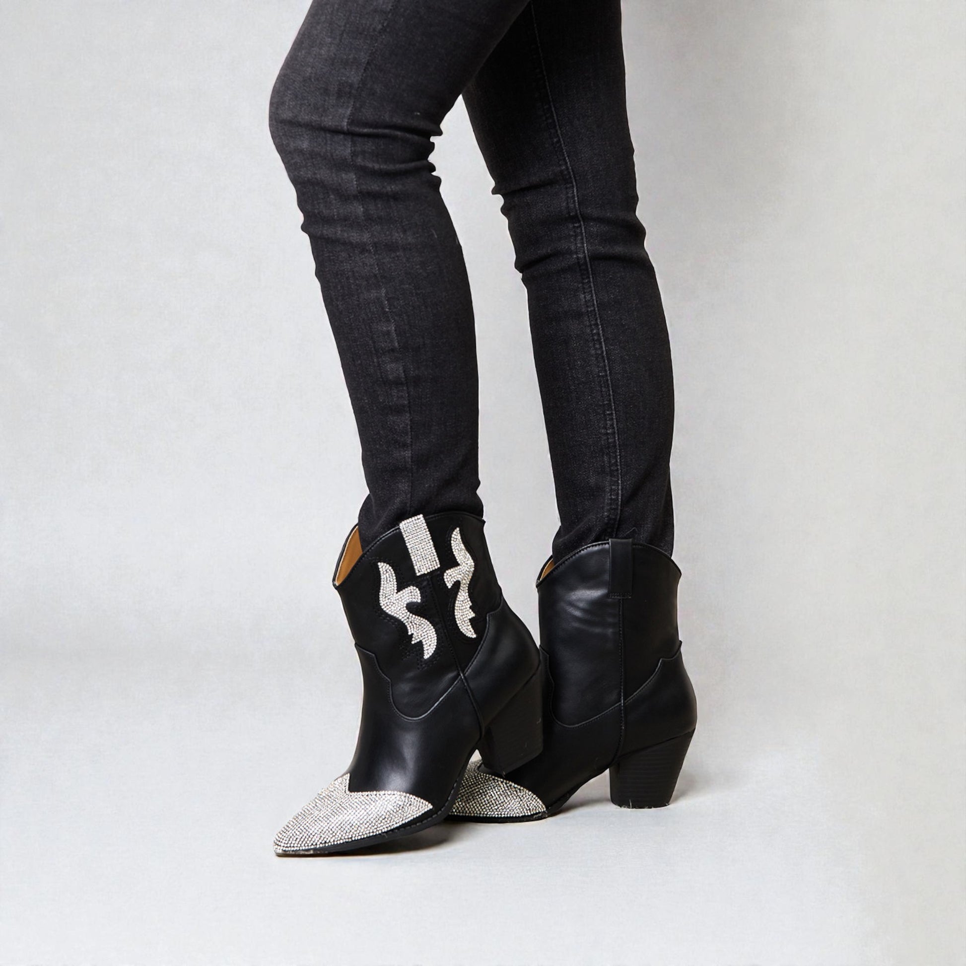 Black cowboy boots with silver embellishments worn with black jeans on a white background