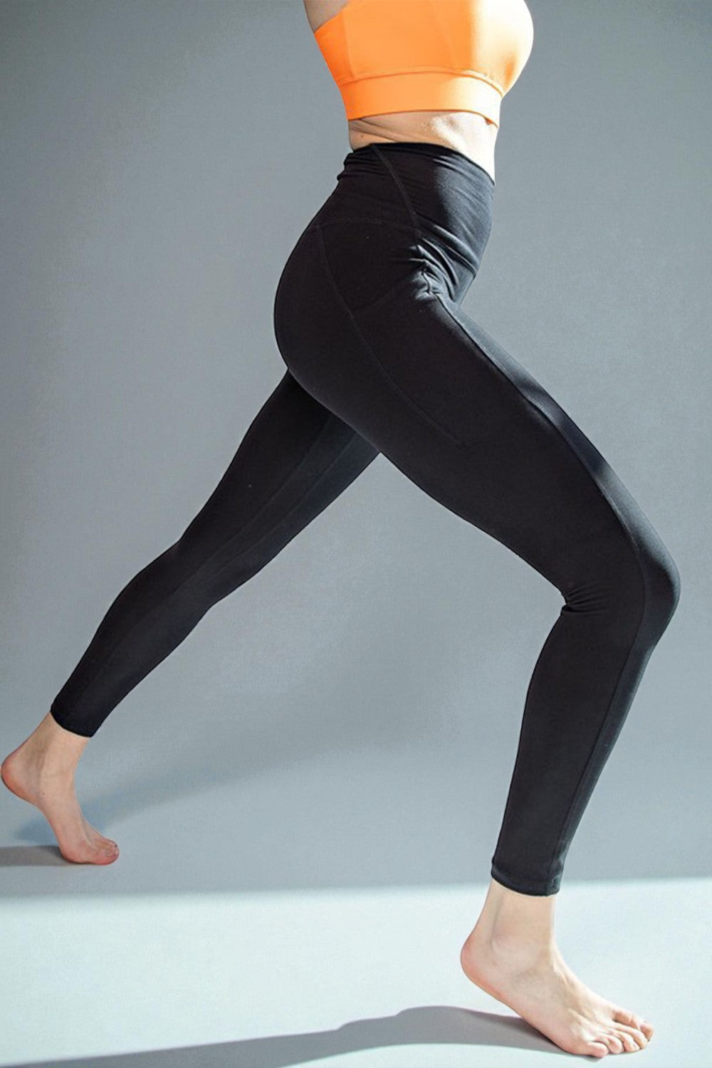 Person wearing black leggings and an orange top on a gray background