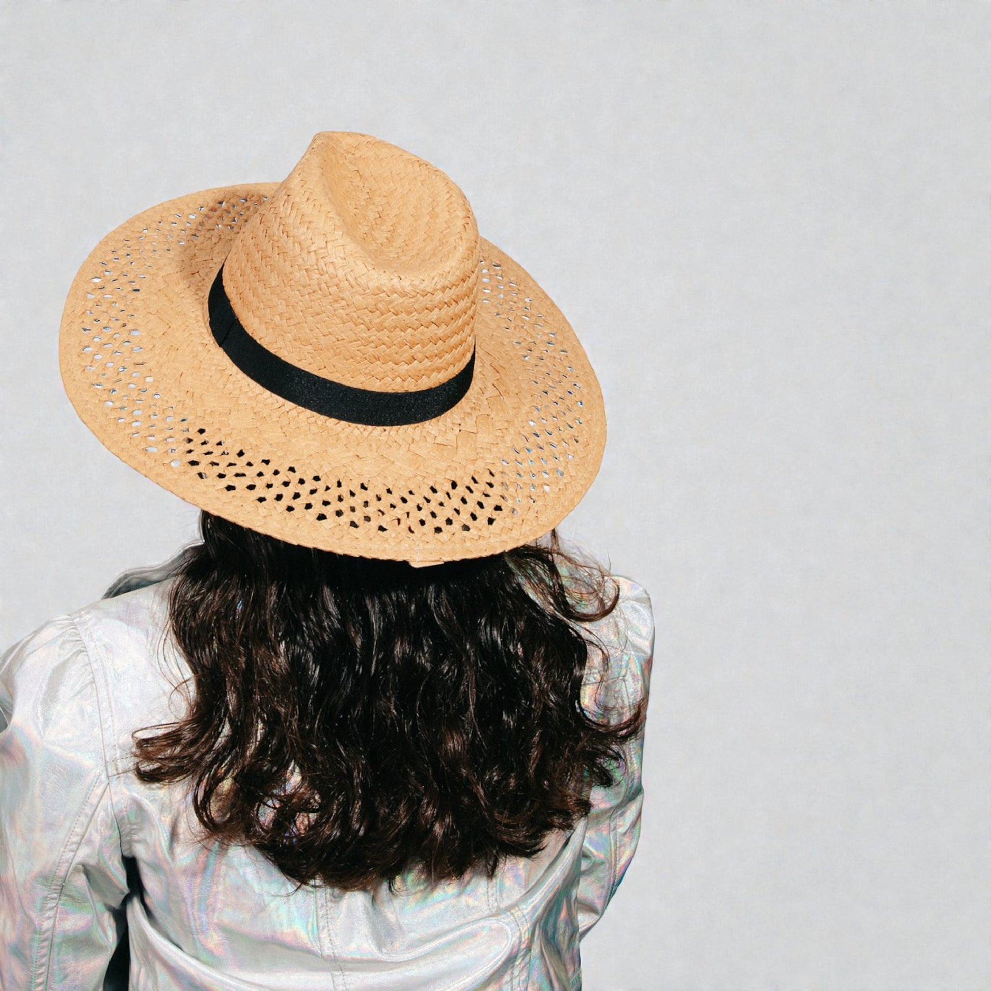 Person wearing a straw hat with a black band on a plain background