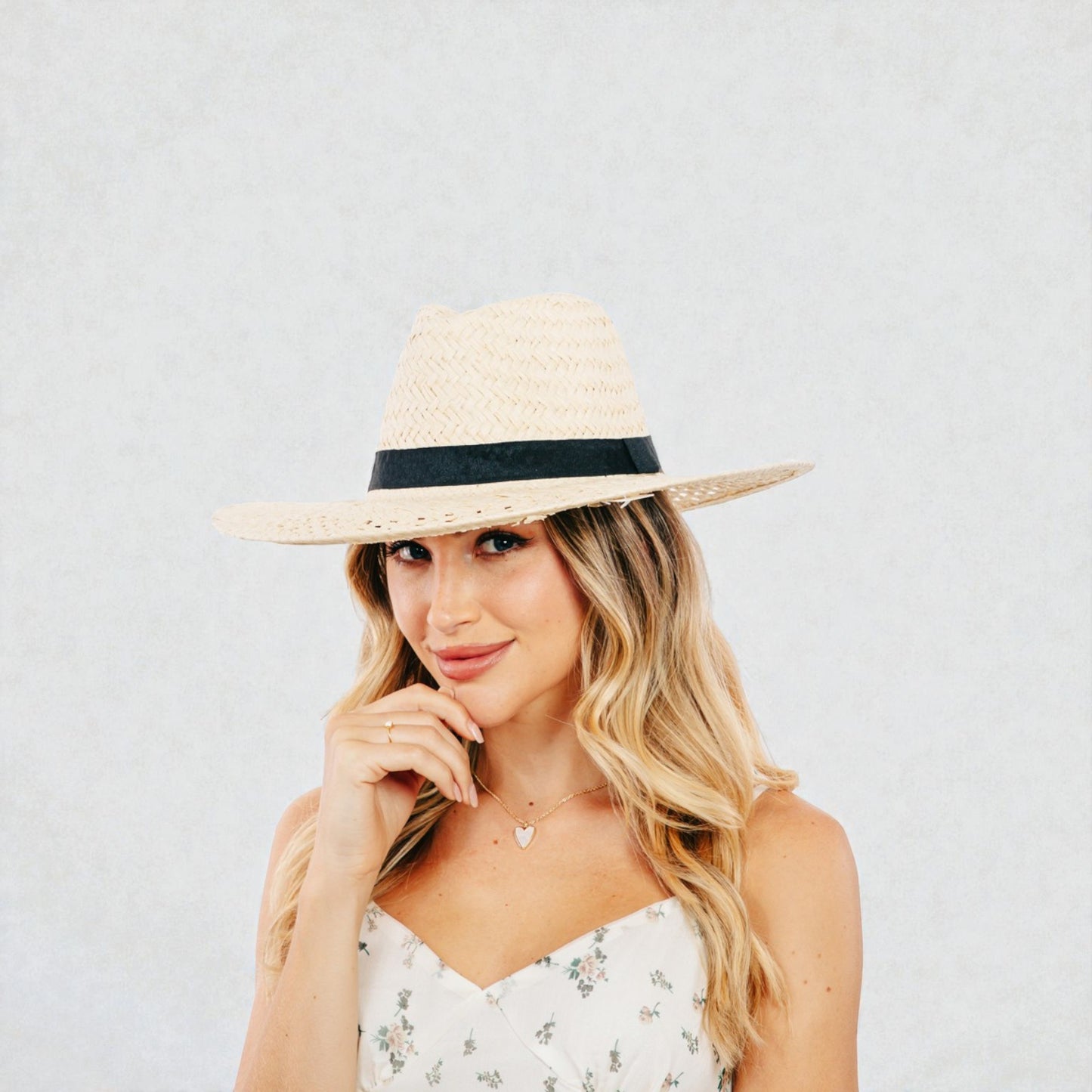 Woman wearing a straw hat with a black band on a plain background