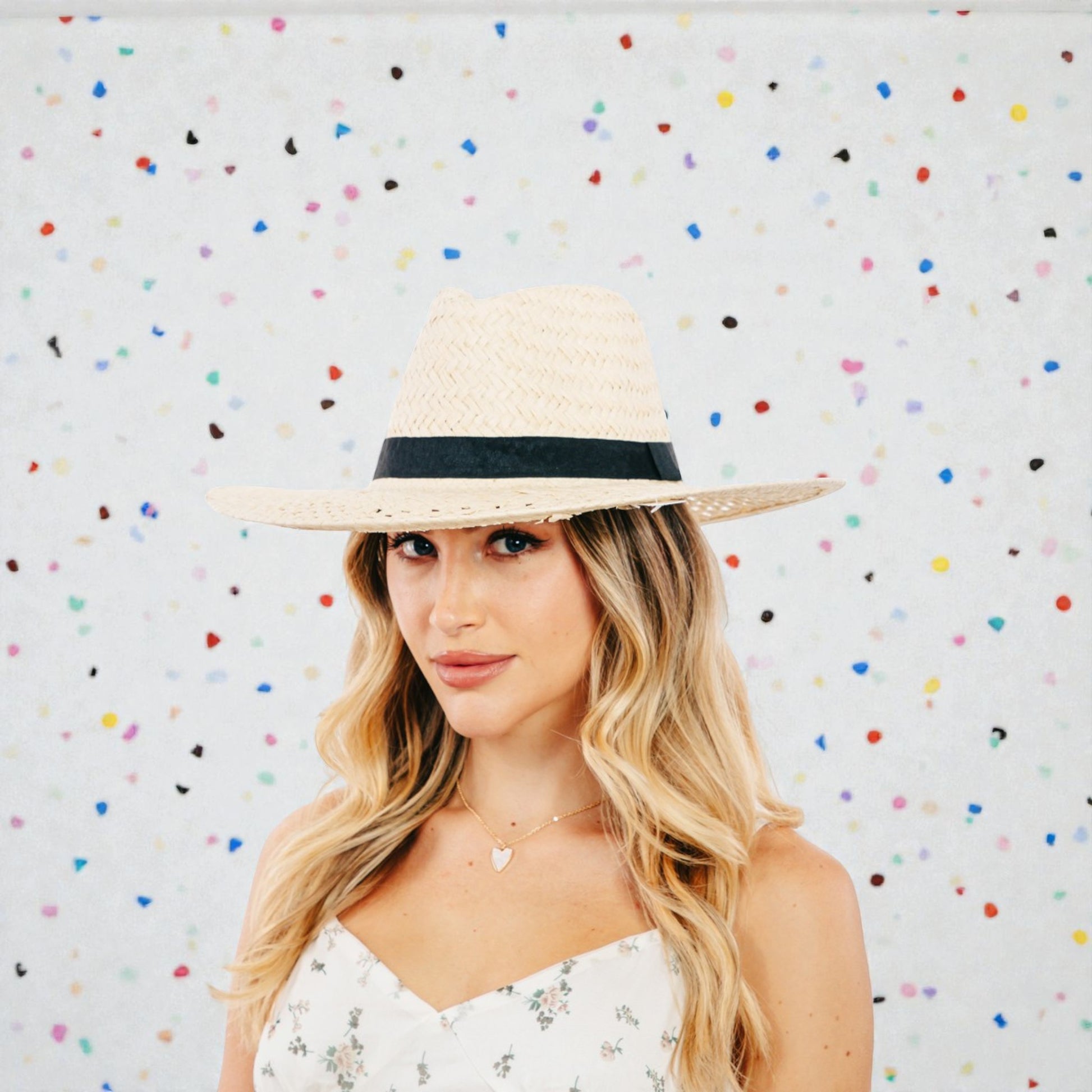Woman wearing a straw hat with a black band against a colorful polka dot background