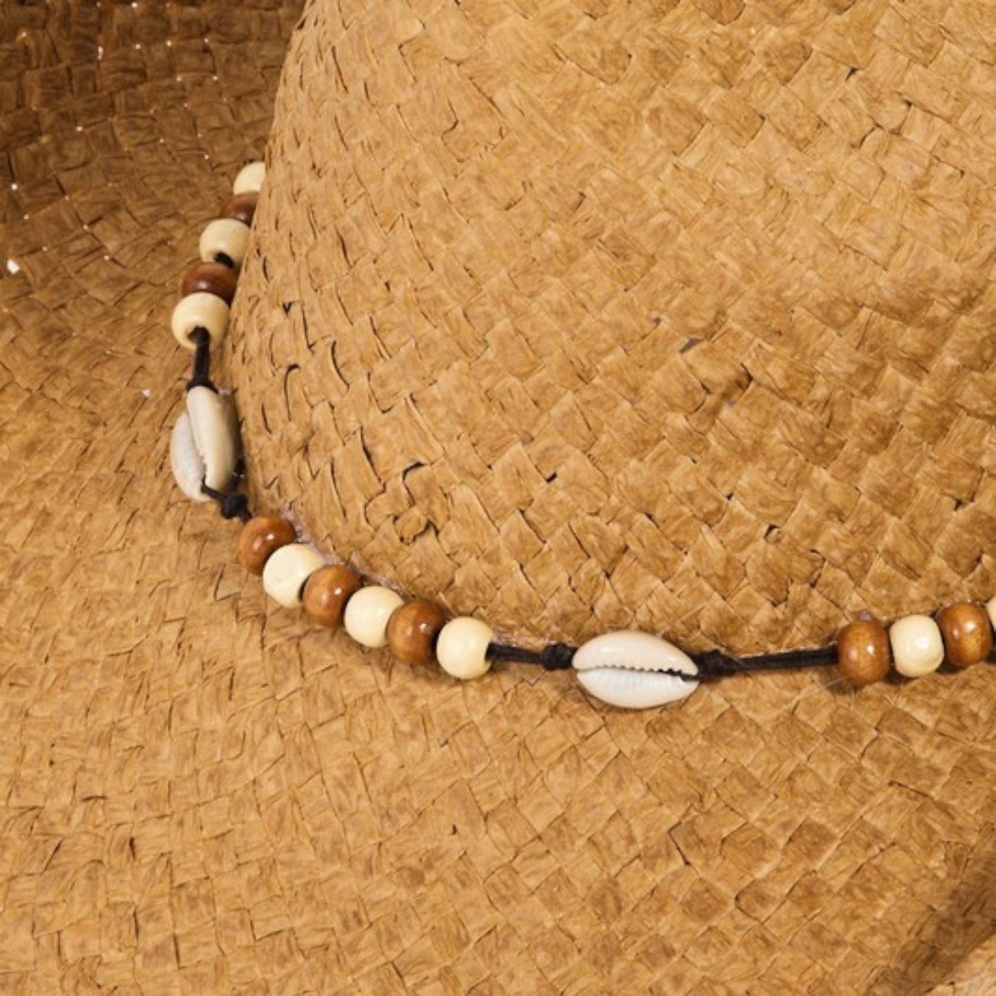 Straw hat with a beaded necklace featuring cowrie shells and wooden beads.