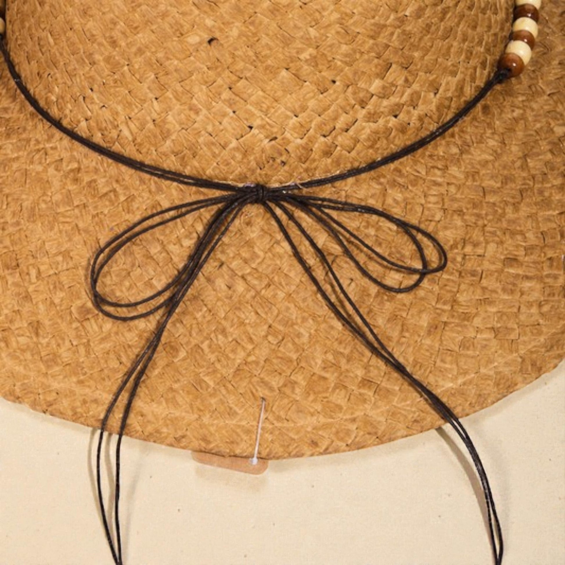 Close-up of a straw hat with a black ribbon and wooden beads on a beige background