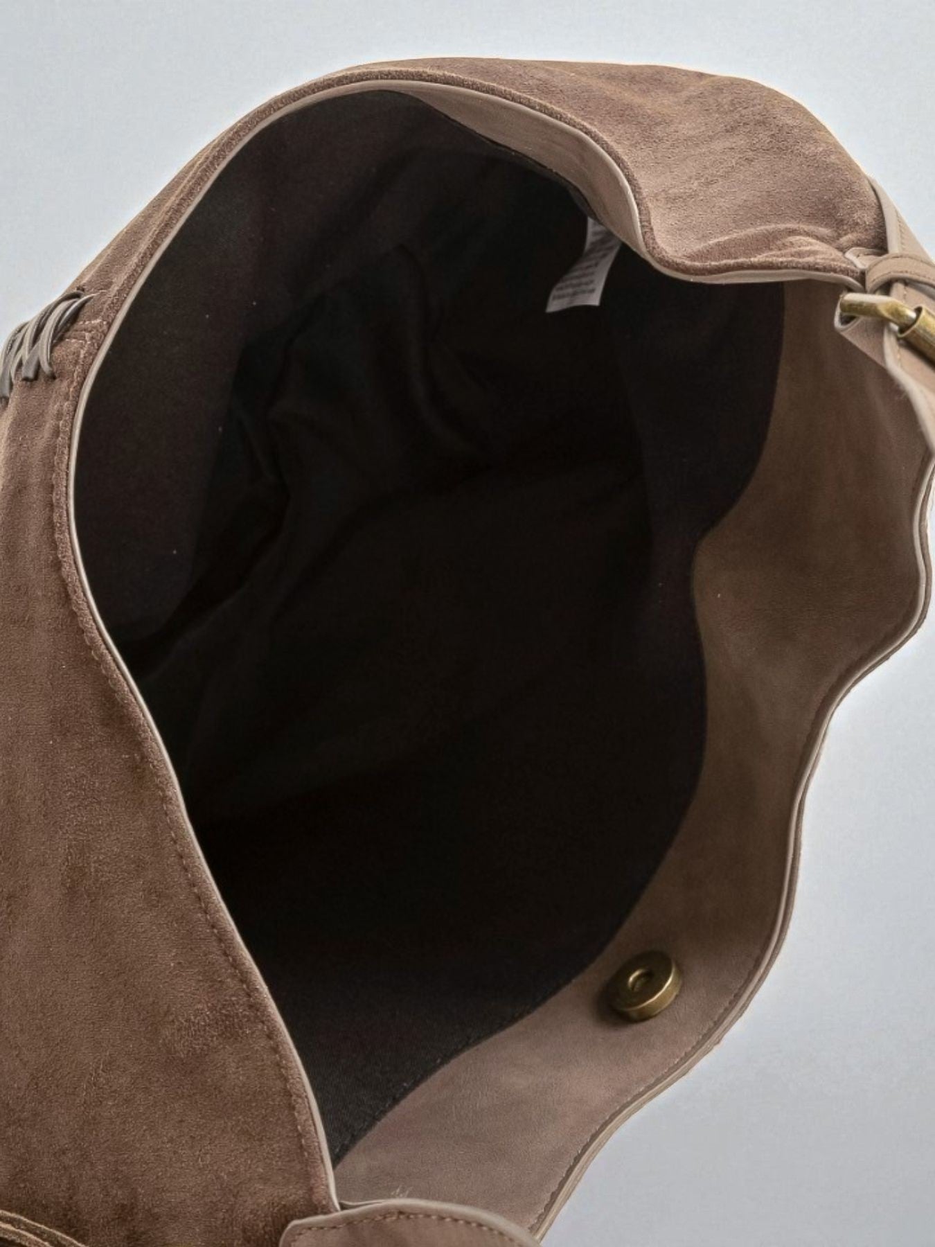 Close-up of a brown leather bag with a visible brand label on a light gray background