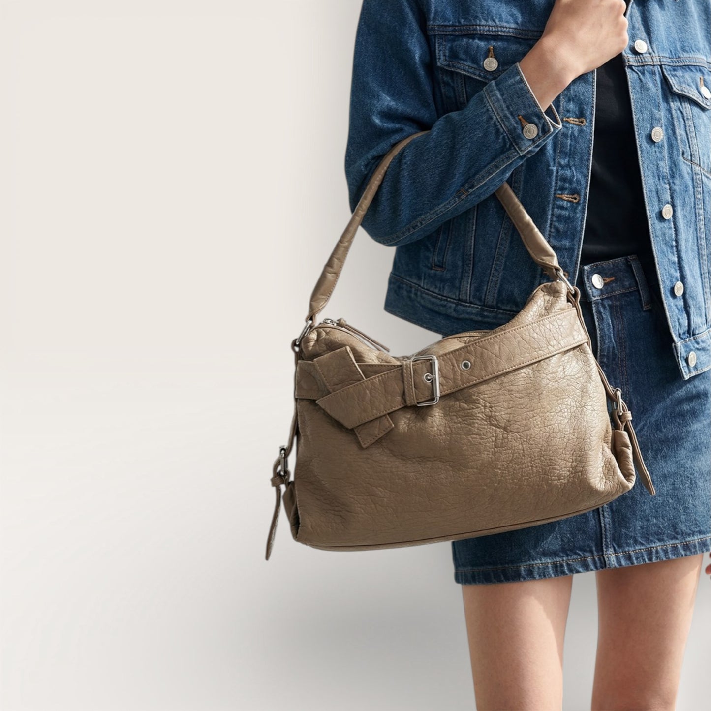 Person wearing a denim jacket and skirt with a brown leather handbag on a plain background