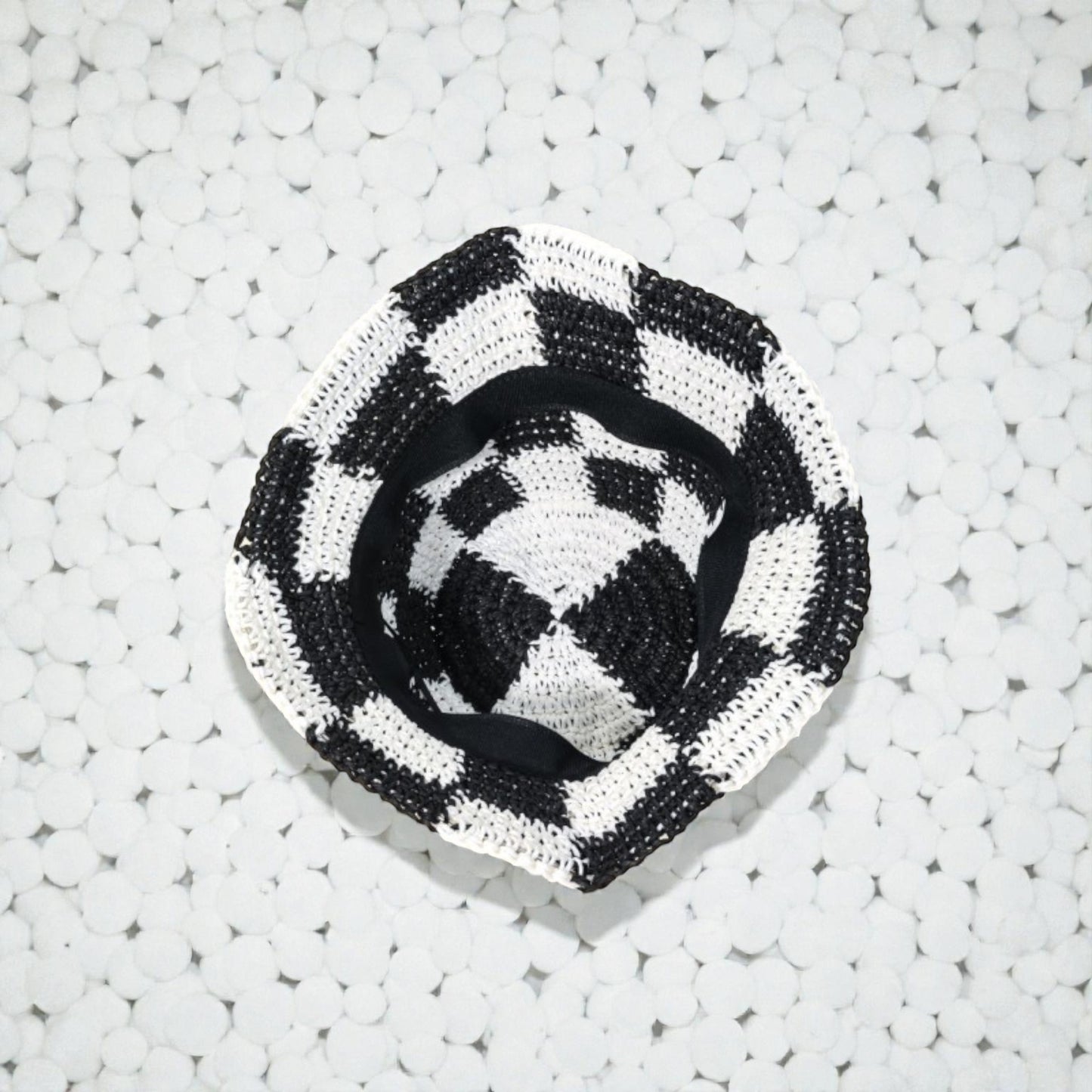 Black and white checkered woven hat on a textured white surface