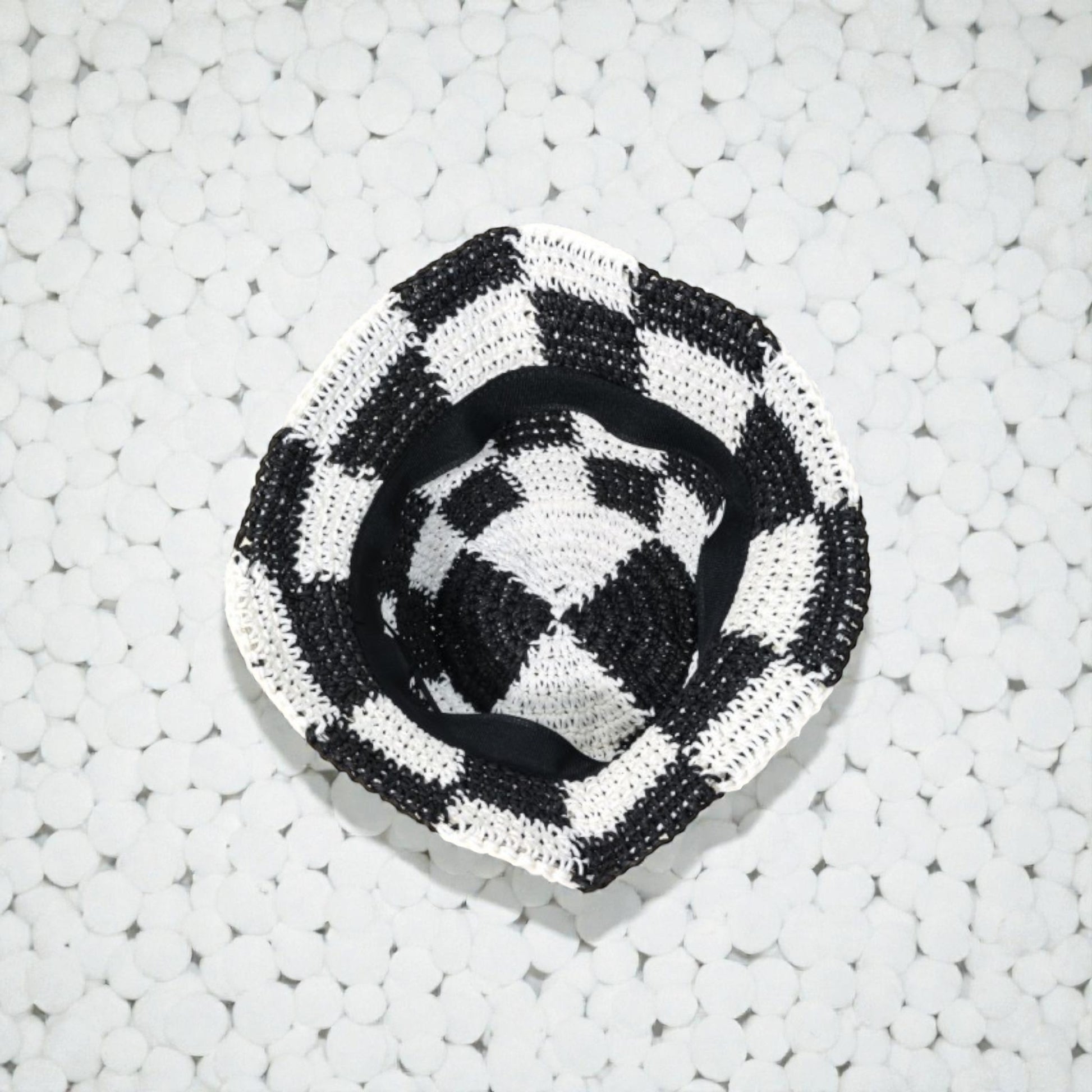 Black and white checkered woven hat on a textured white surface