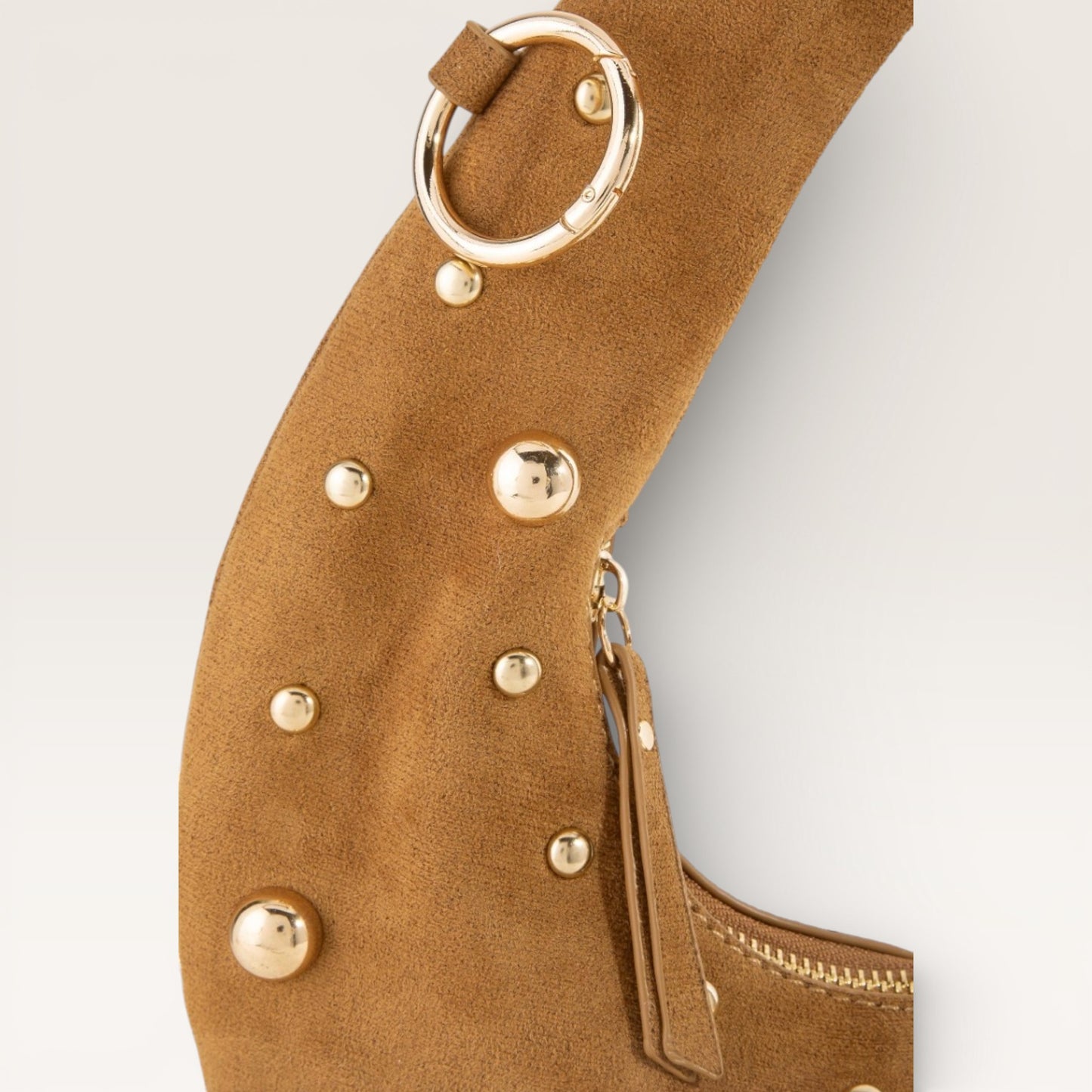 Close-up of a brown leather handbag with gold studs and ring handle on a light gray background