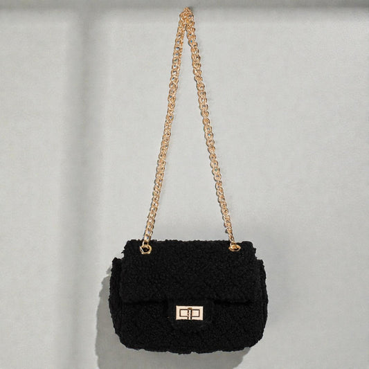Black textured handbag with a gold chain strap on a light gray background