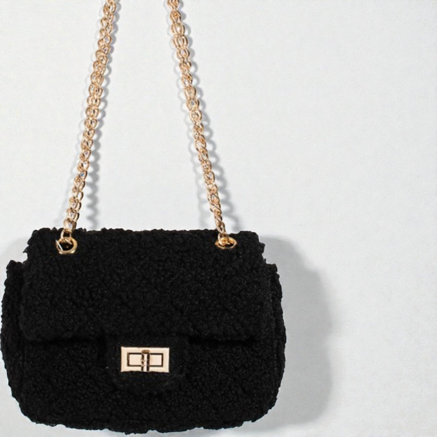 Black textured handbag with gold chain strap on a light gray background