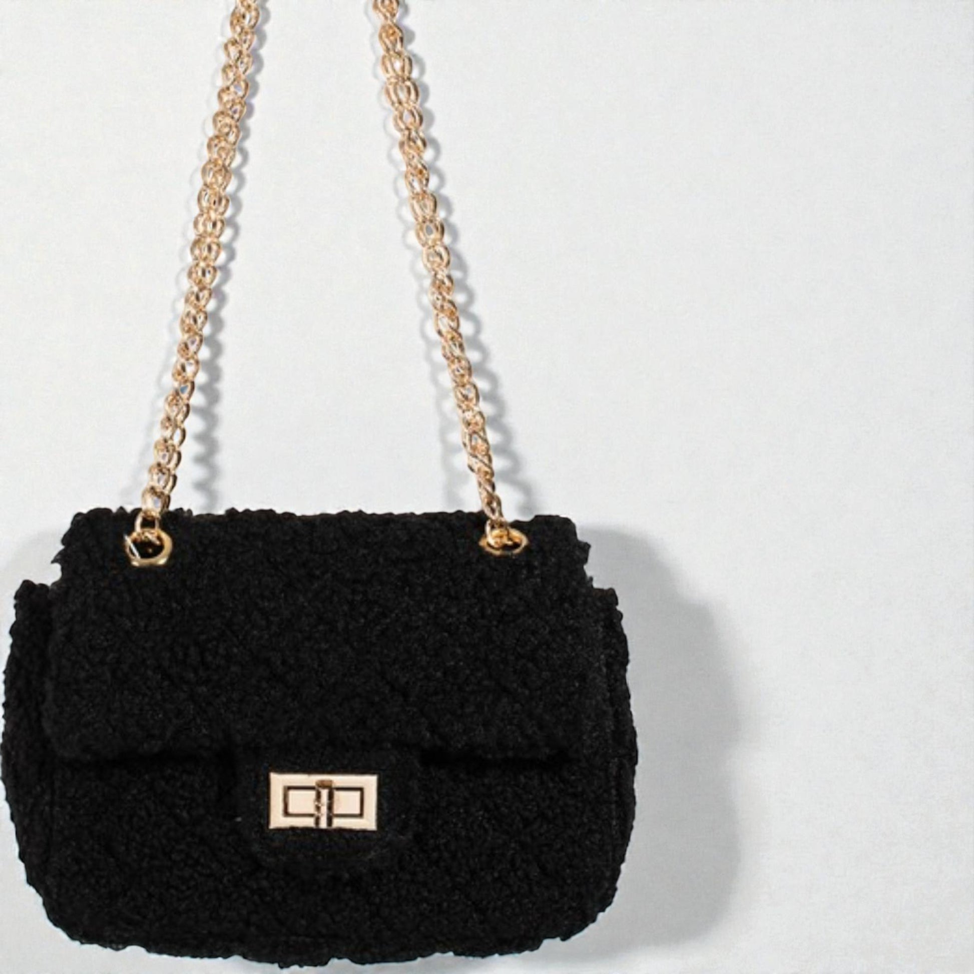Black textured handbag with gold chain strap on a light gray background