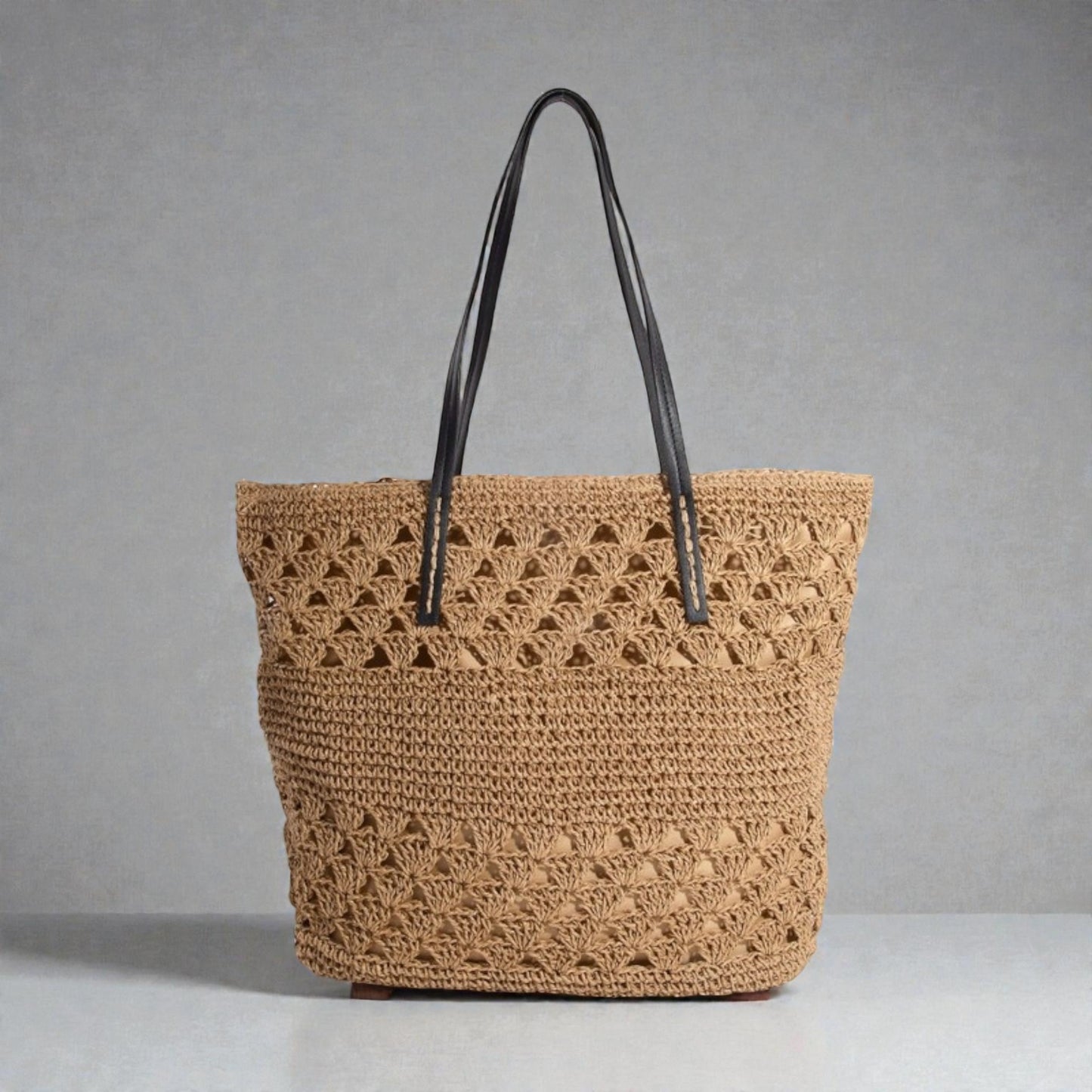 Brown woven tote bag with black handles on a gray background