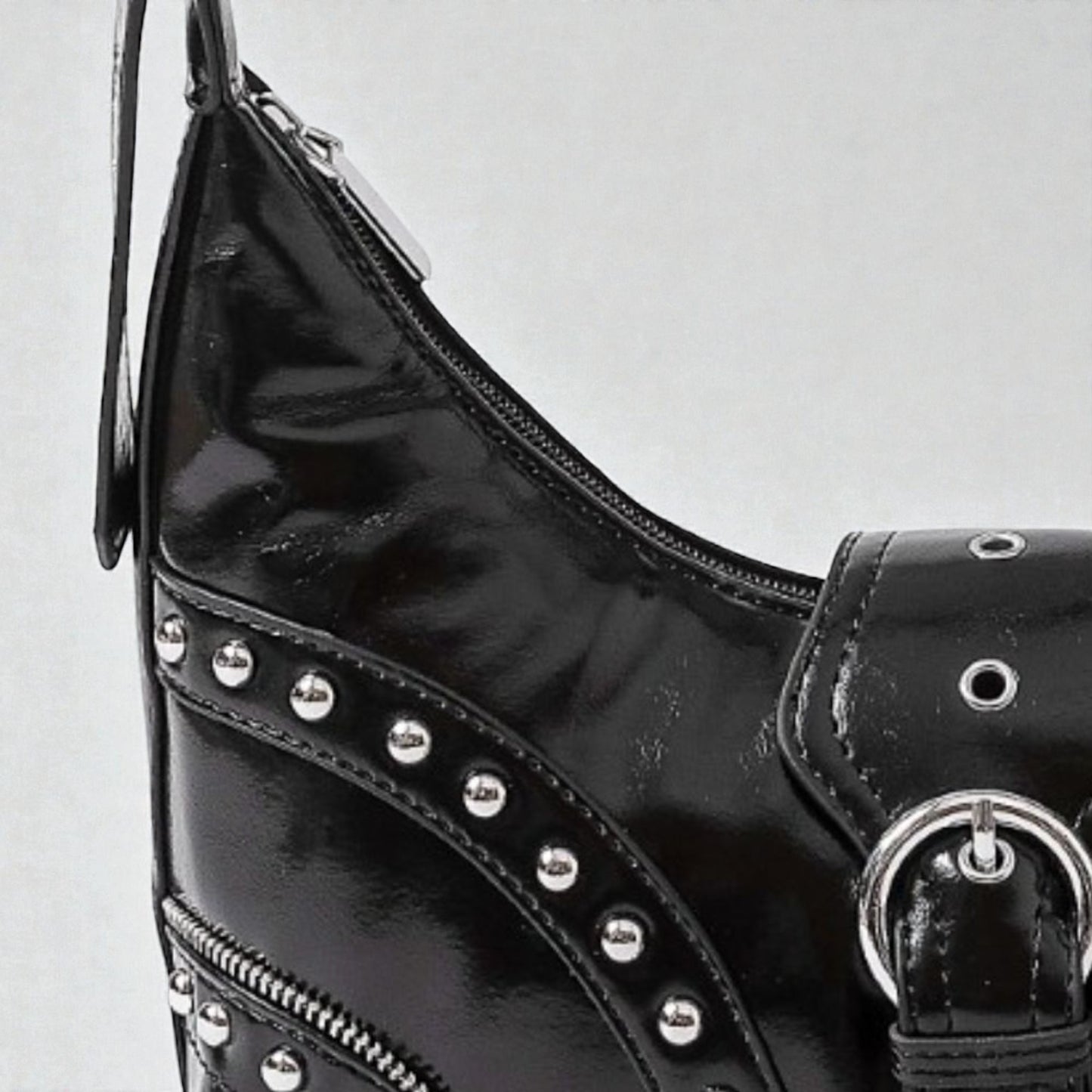 Black patent leather handbag with silver studs and a ring detail on a light gray background