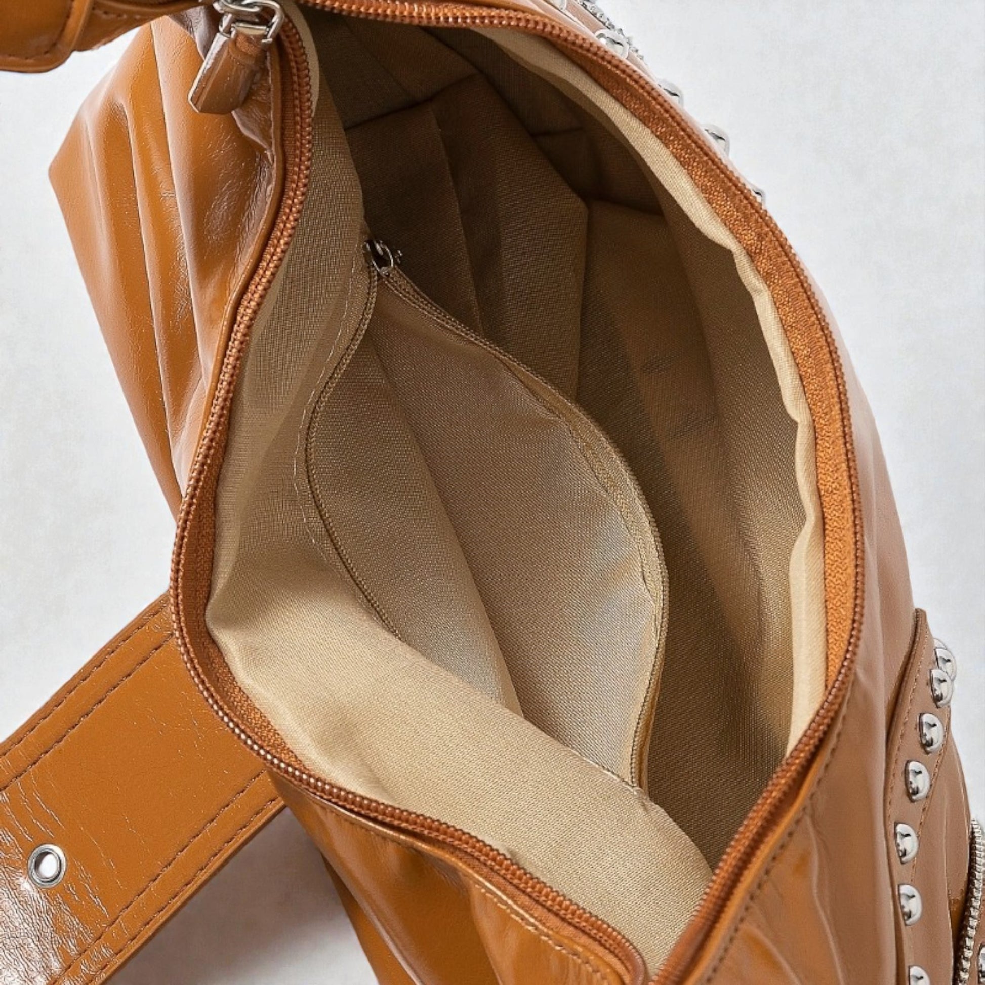 Close-up of a brown leather handbag with studded details on a light gray background