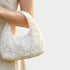 White textured handbag held by a person against a light background
