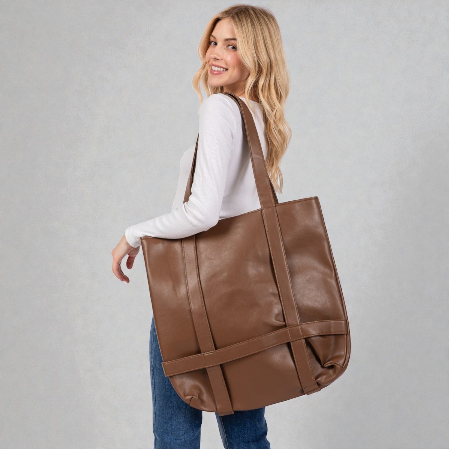 Woman carrying a brown leather tote bag against a plain background