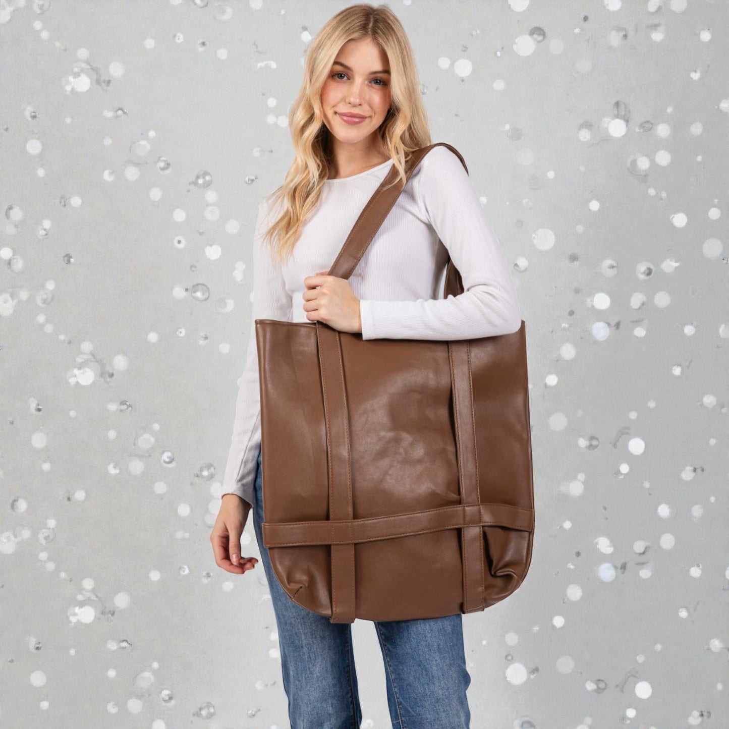 Woman holding a brown leather tote bag against a gray background with white circular patterns