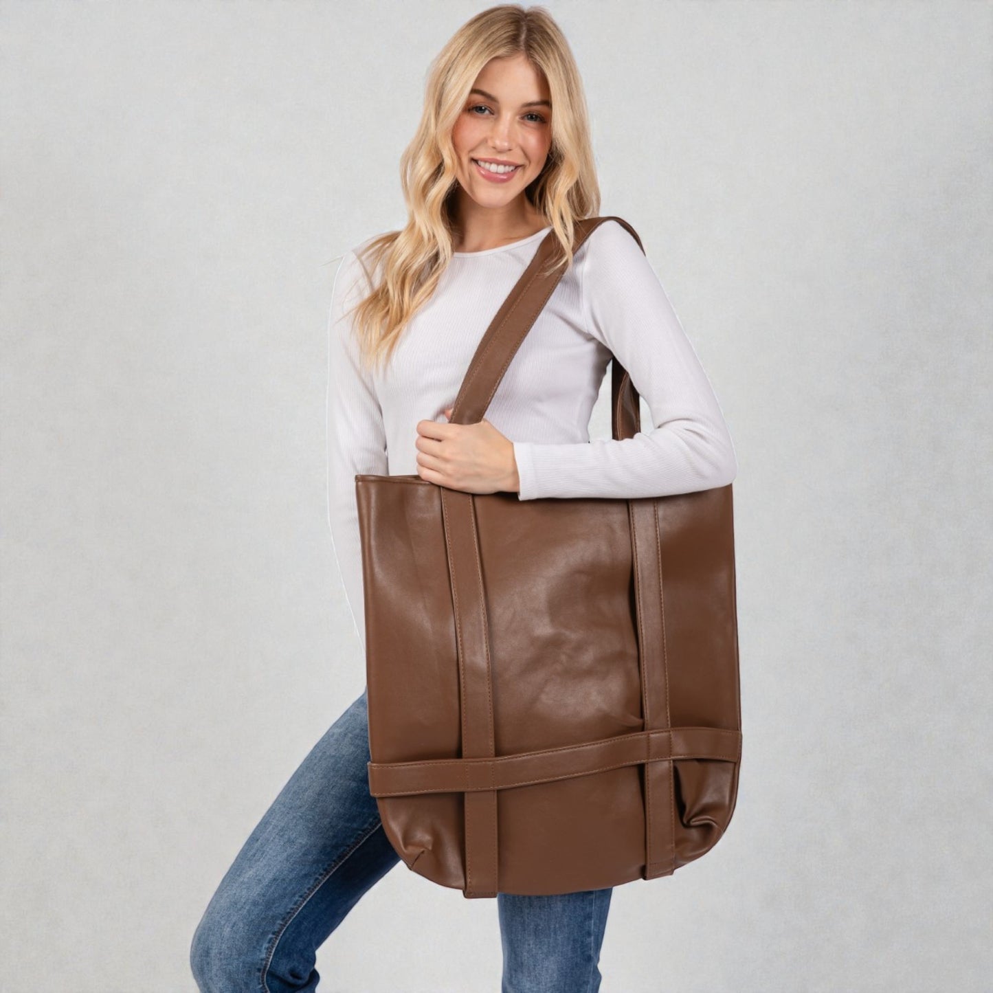 Woman holding a brown leather tote bag against a plain background