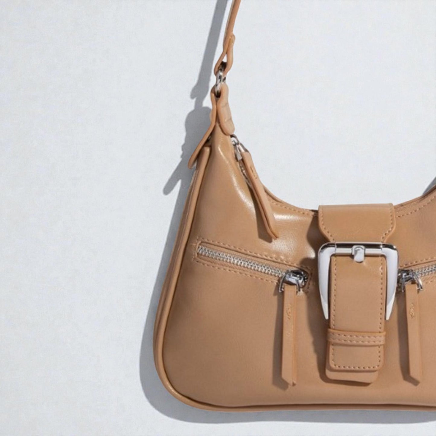 Tan handbag with a silver buckle on a light gray background