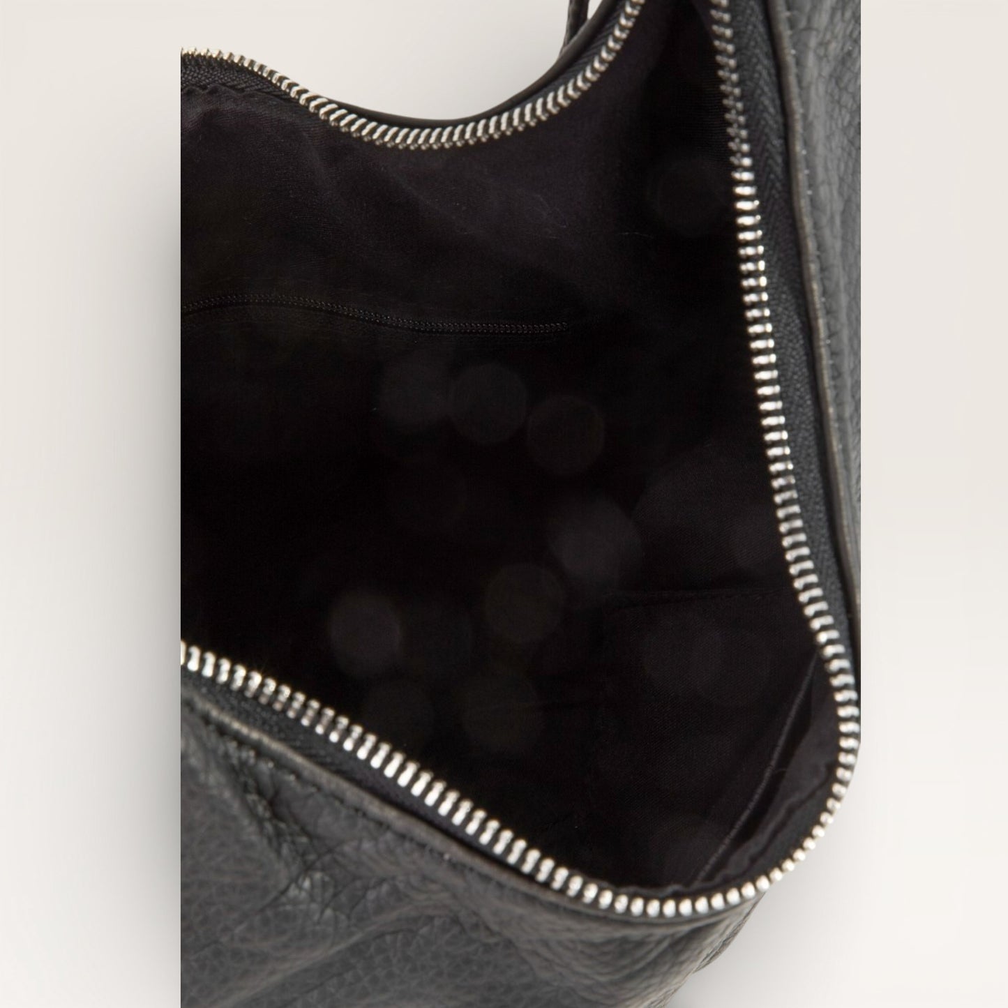 Close-up of a black leather bag with a zipper on a light gray background