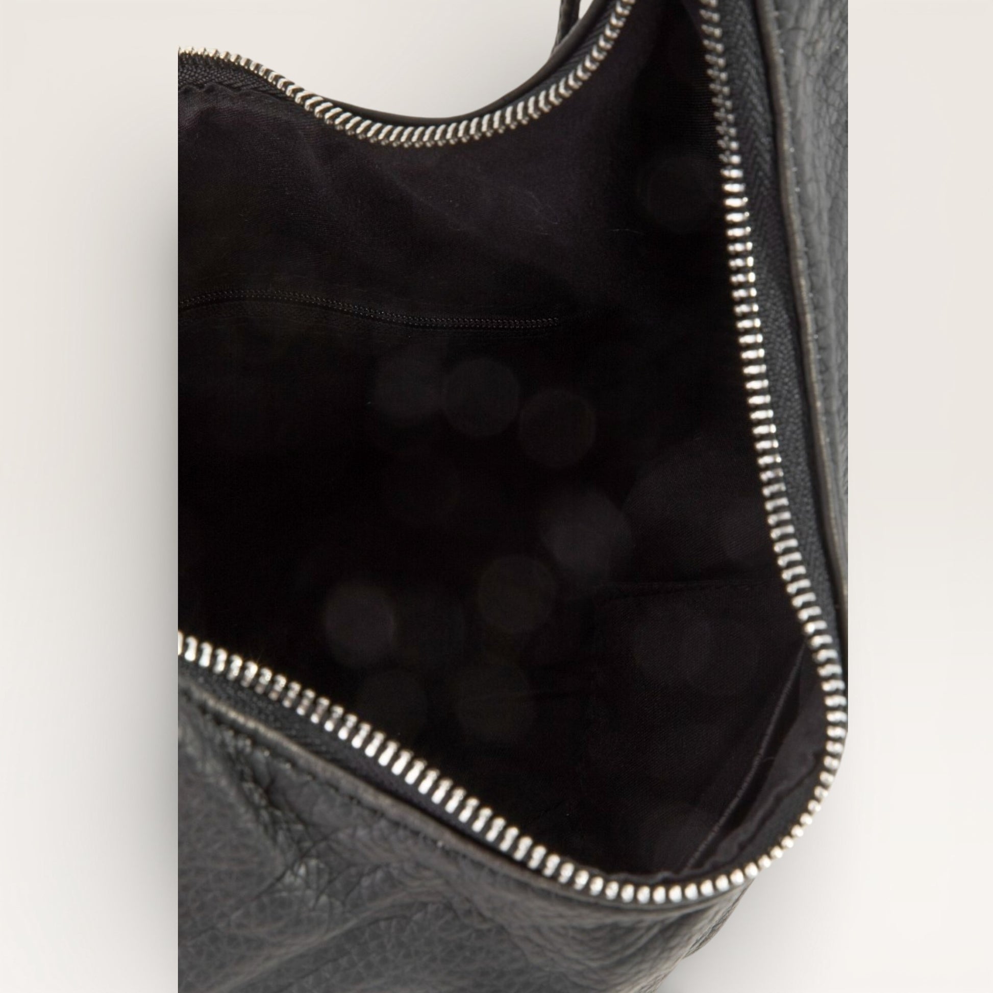 Close-up of a black leather bag with a zipper on a light gray background