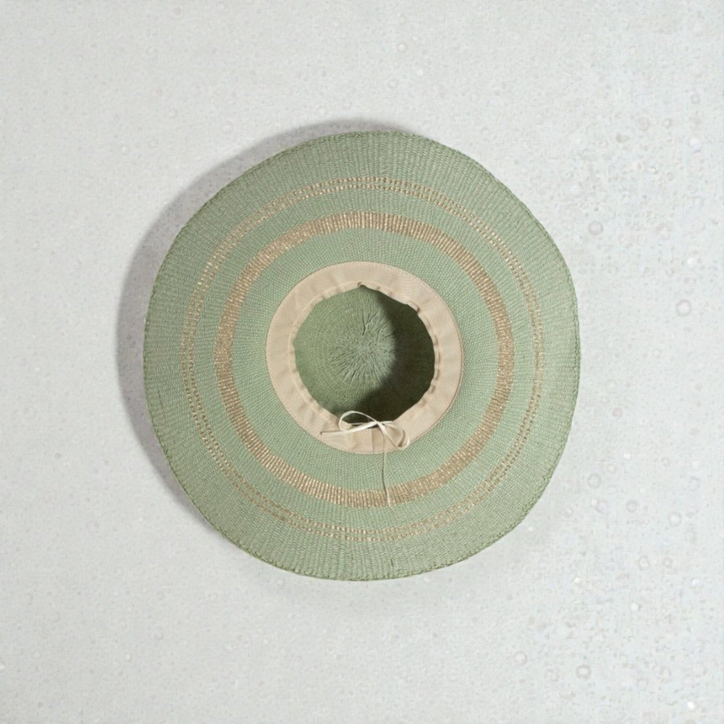 Green sun hat with beige band on a textured light gray background