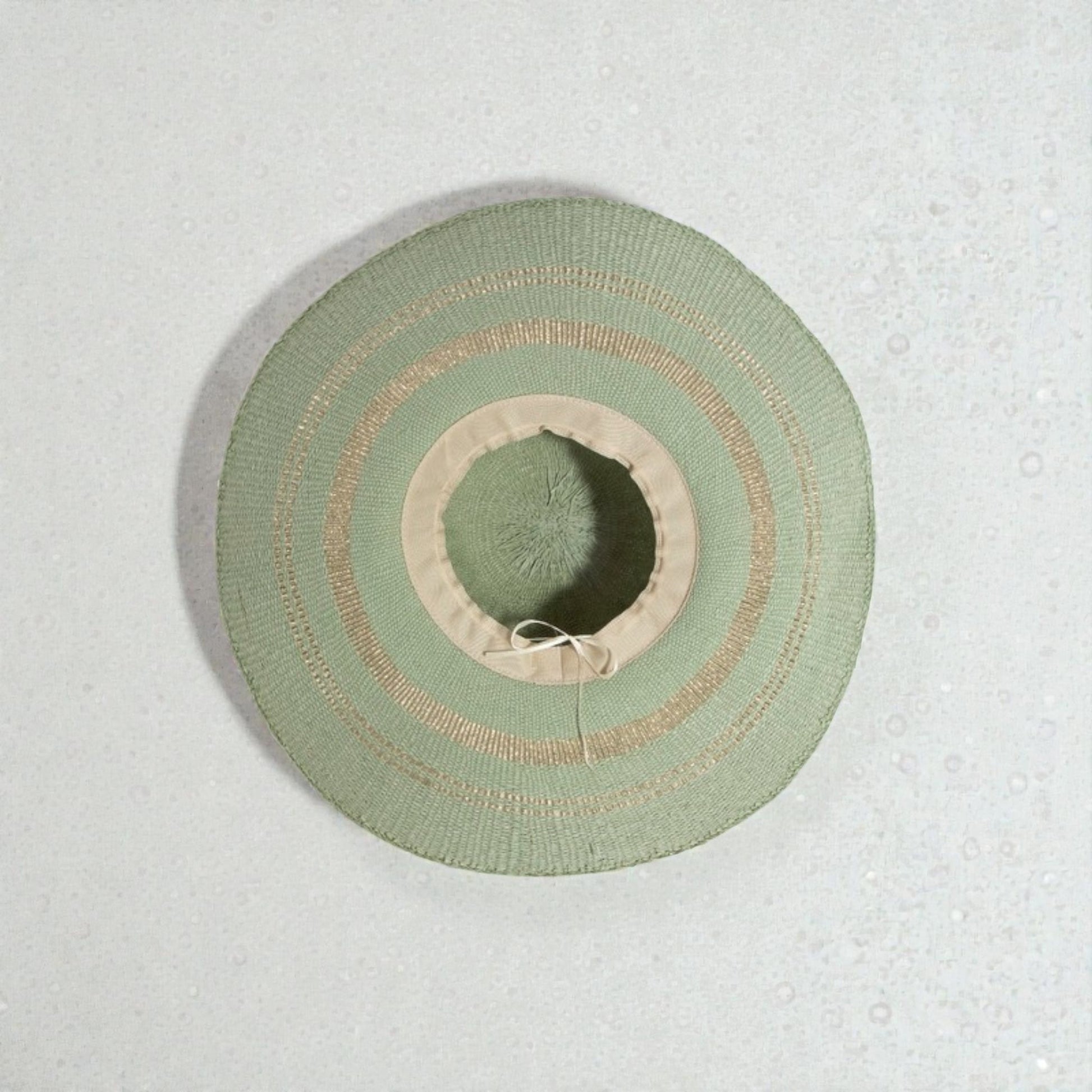 Green sun hat with beige band on a textured light gray background
