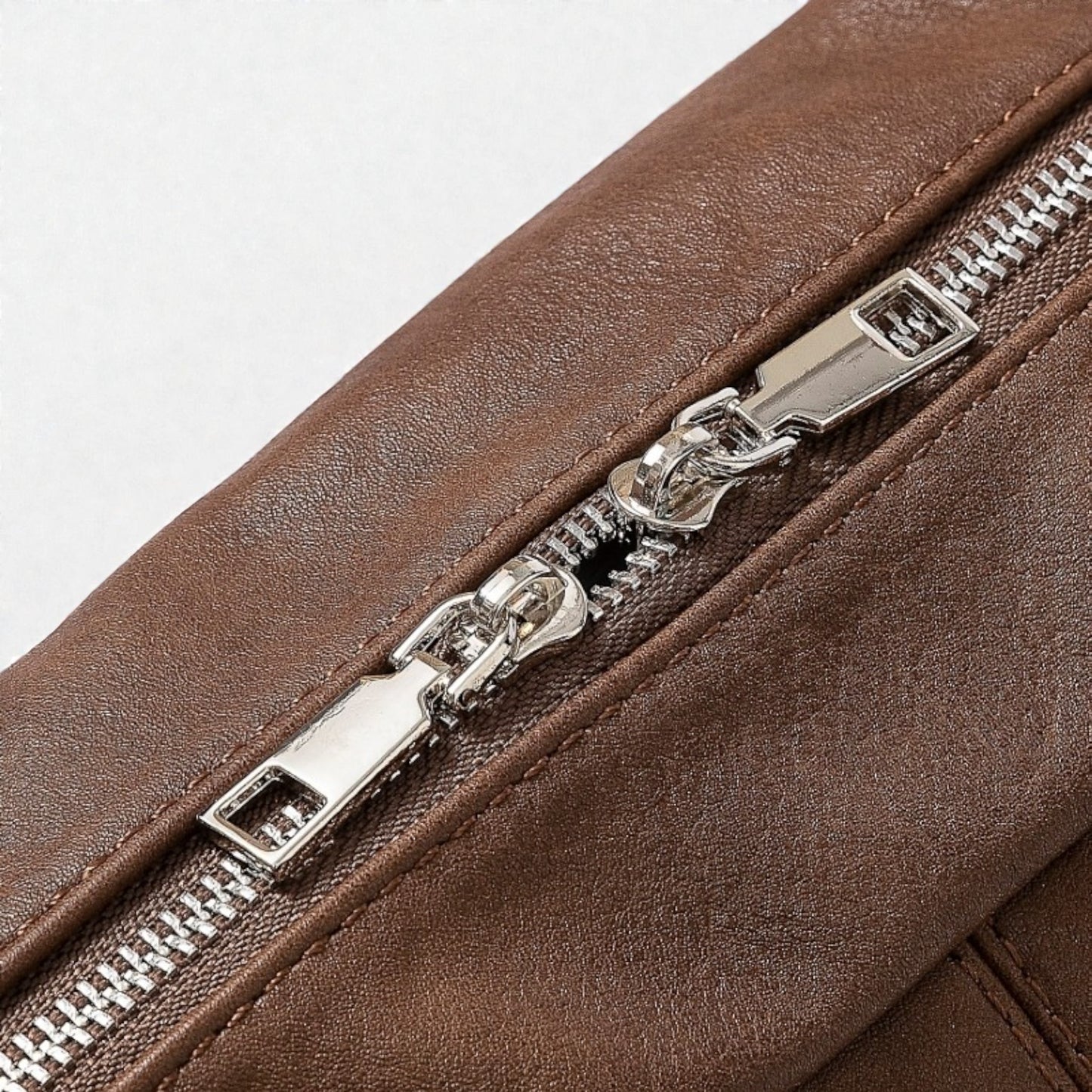 Close-up of a brown leather bag with a silver zipper on a light gray background